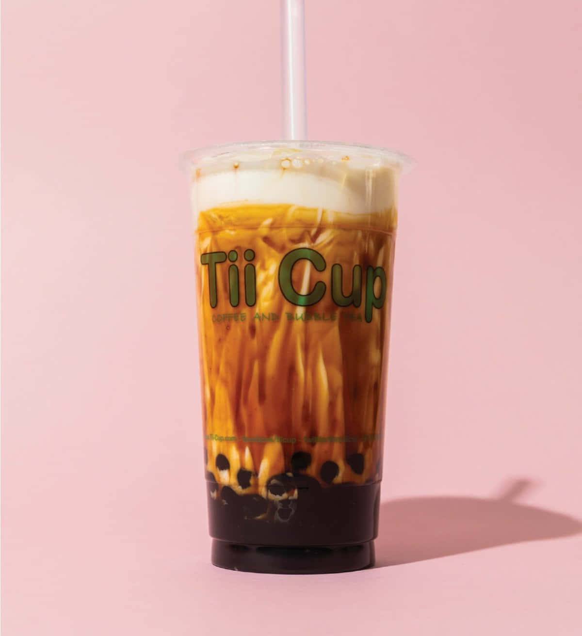 Boba Tea 桌布 壁紙 — 一杯高身冰咖啡泡泡茶，帶有奶油泡沫和黑珍珠，放在品牌杯中，背景是柔和的粉紅色。