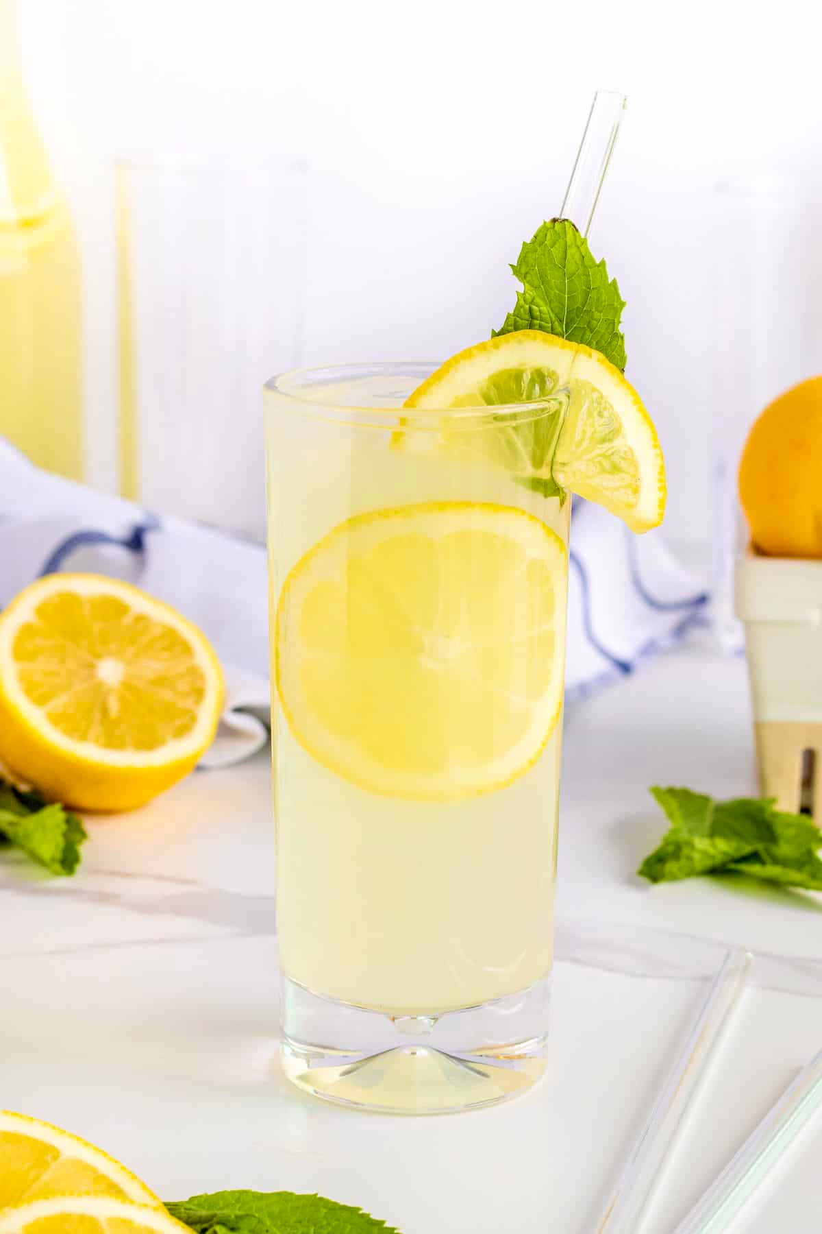 Lemonade 桌布 壁紙 — 一杯高身清涼檸檬水，飾以檸檬片和薄荷葉，放在明亮的白色表面上。
