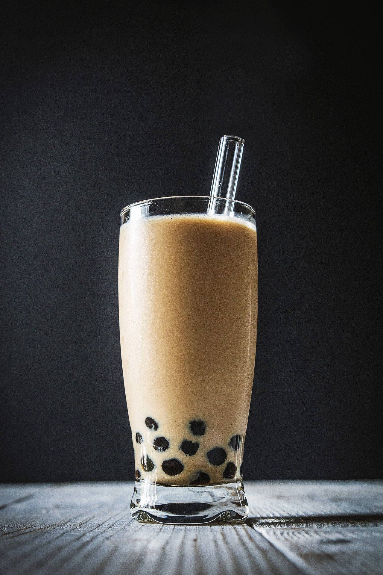Bubble 桌布 壁紙 — 一杯高身的奶油泡泡茶搭配黑色木薯珍珠，放在深色背景的鄉村風格木桌上。