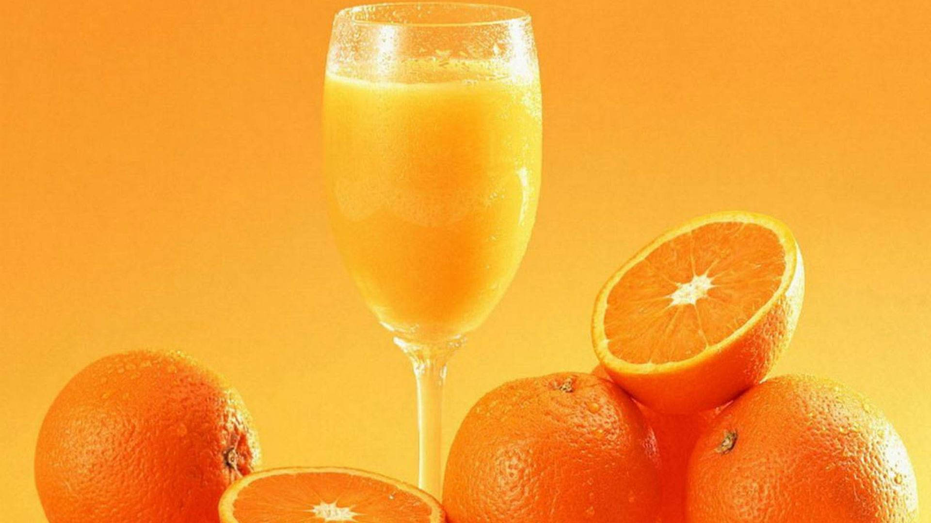 Orange Fruit 桌布 壁紙 — 一杯高身的新鮮柳橙汁，周圍放著完整和切片的柳橙，背景是溫暖的橙色漸層。