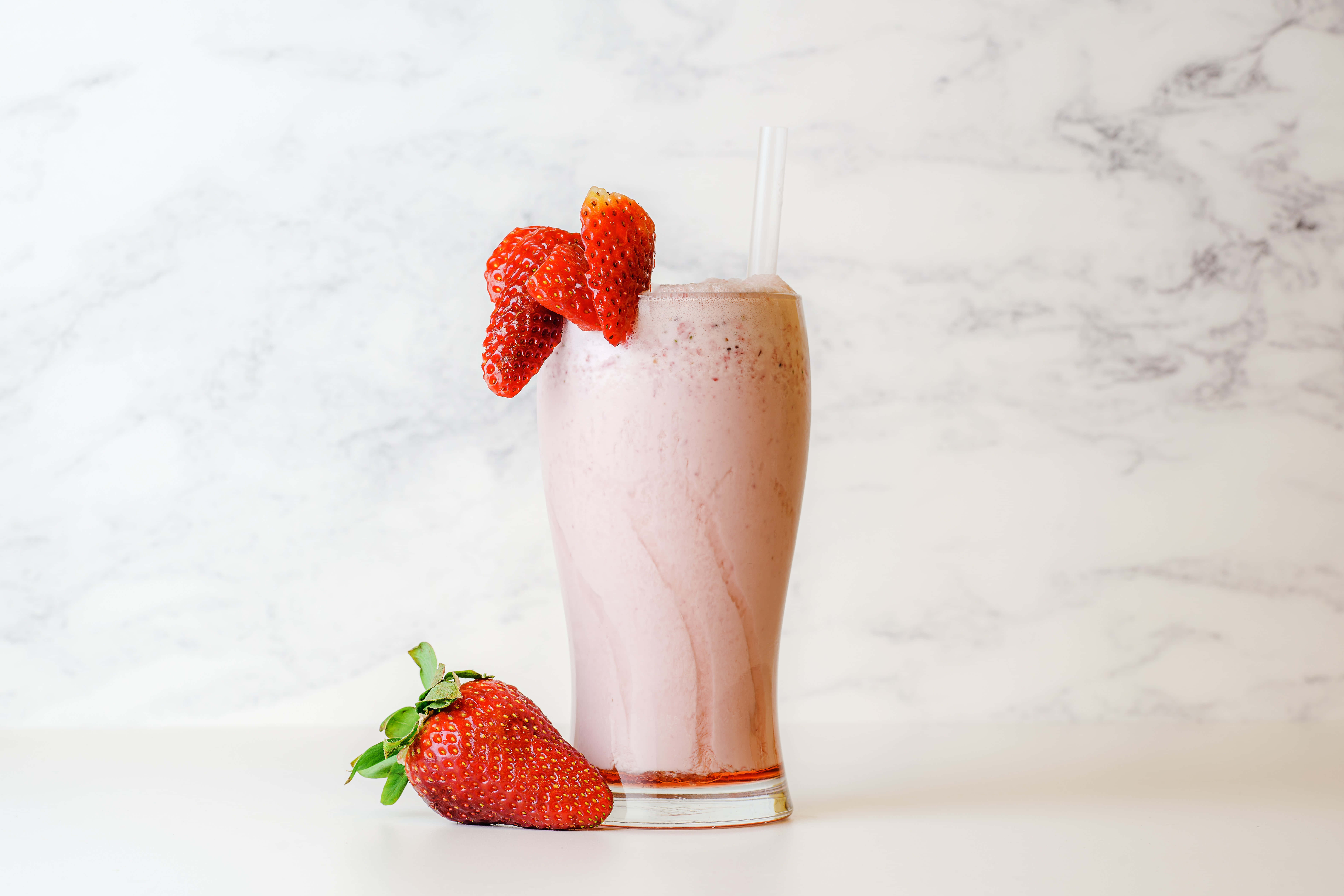 Summer Drinks 桌布 壁紙 — 一杯高身粉紅草莓奶昔，以新鮮草莓點綴，襯以白色大理石背景。