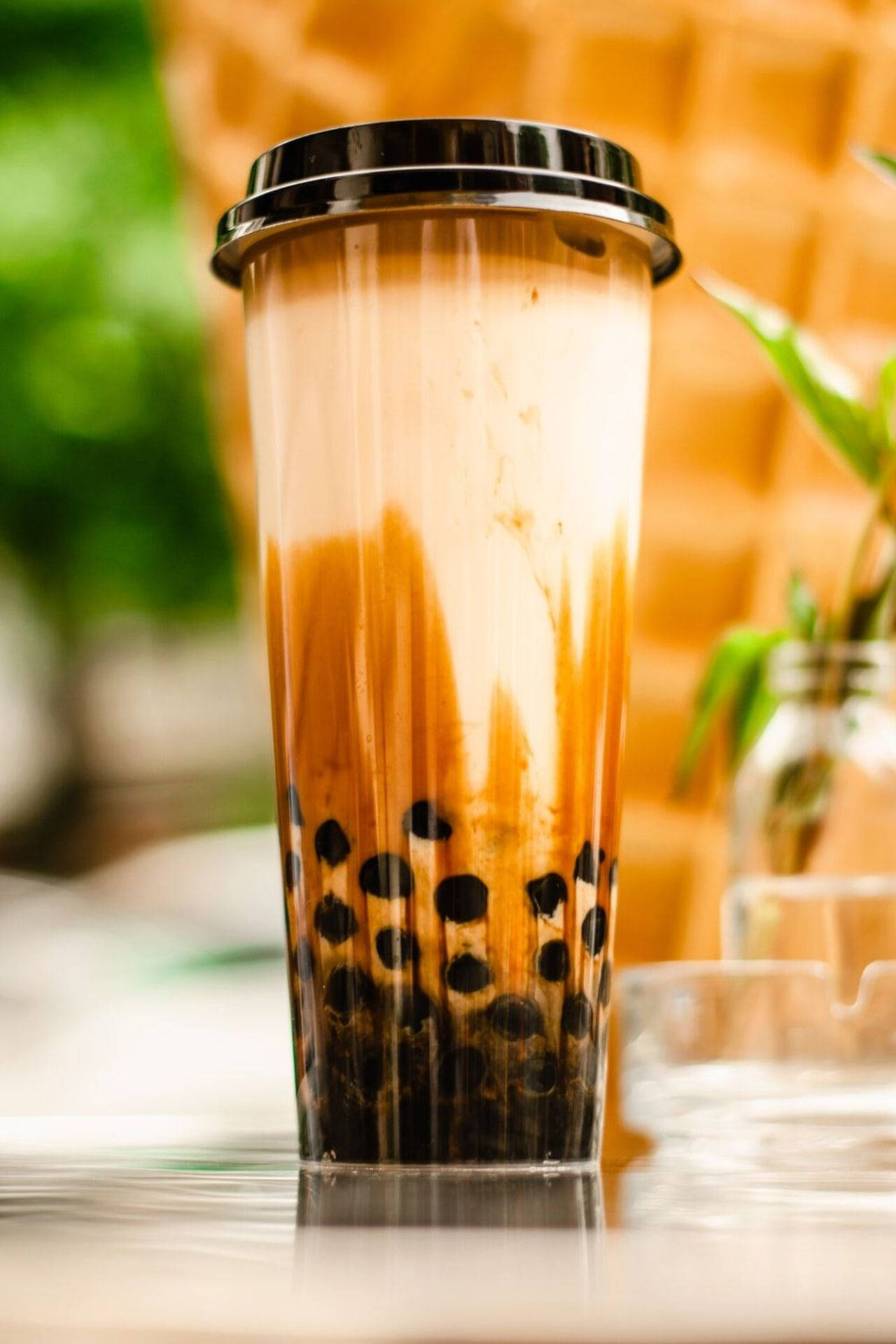 Bubble 桌布 壁紙 — 一杯高身透明杯裝著 creamy 焦糖泡泡茶，配以黑色木薯珍珠，放在反光表面上，背景溫暖模糊。