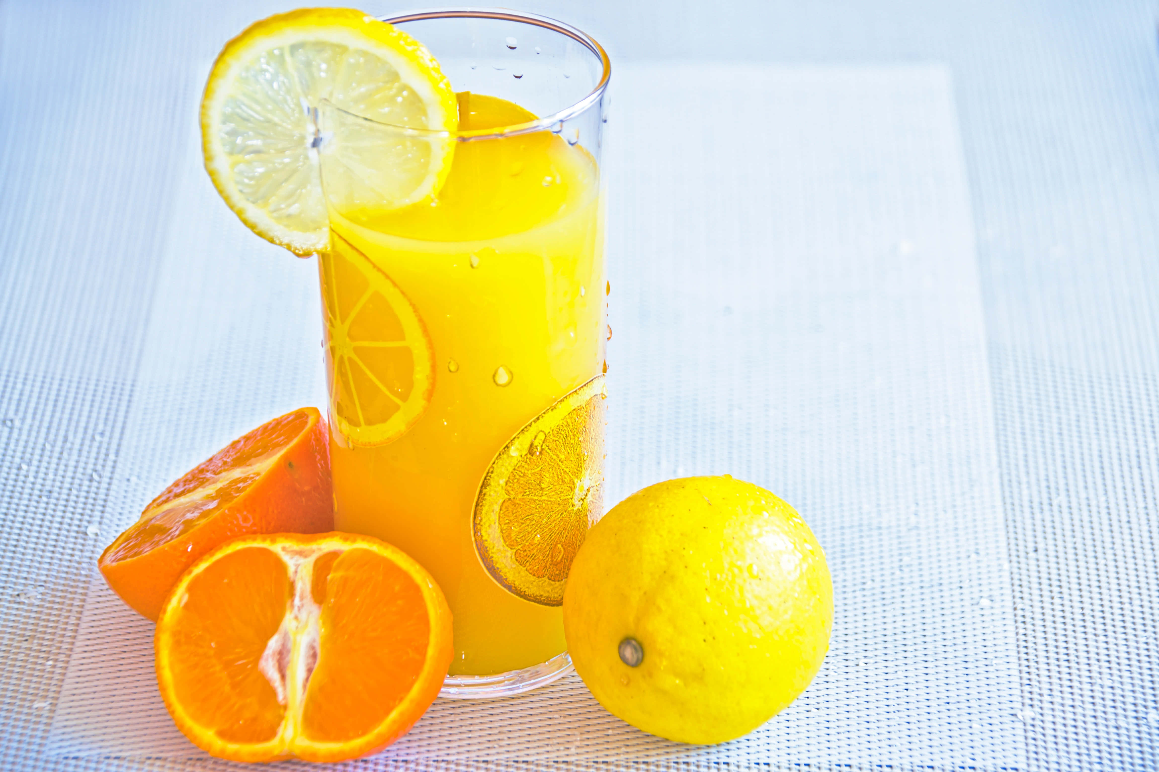 Summer Drinks 桌布 壁紙 — 一杯高身鮮橙汁，飾以檸檬和柳橙片，旁邊放上新鮮柑橘類水果，置於有紋理的白色表面上。