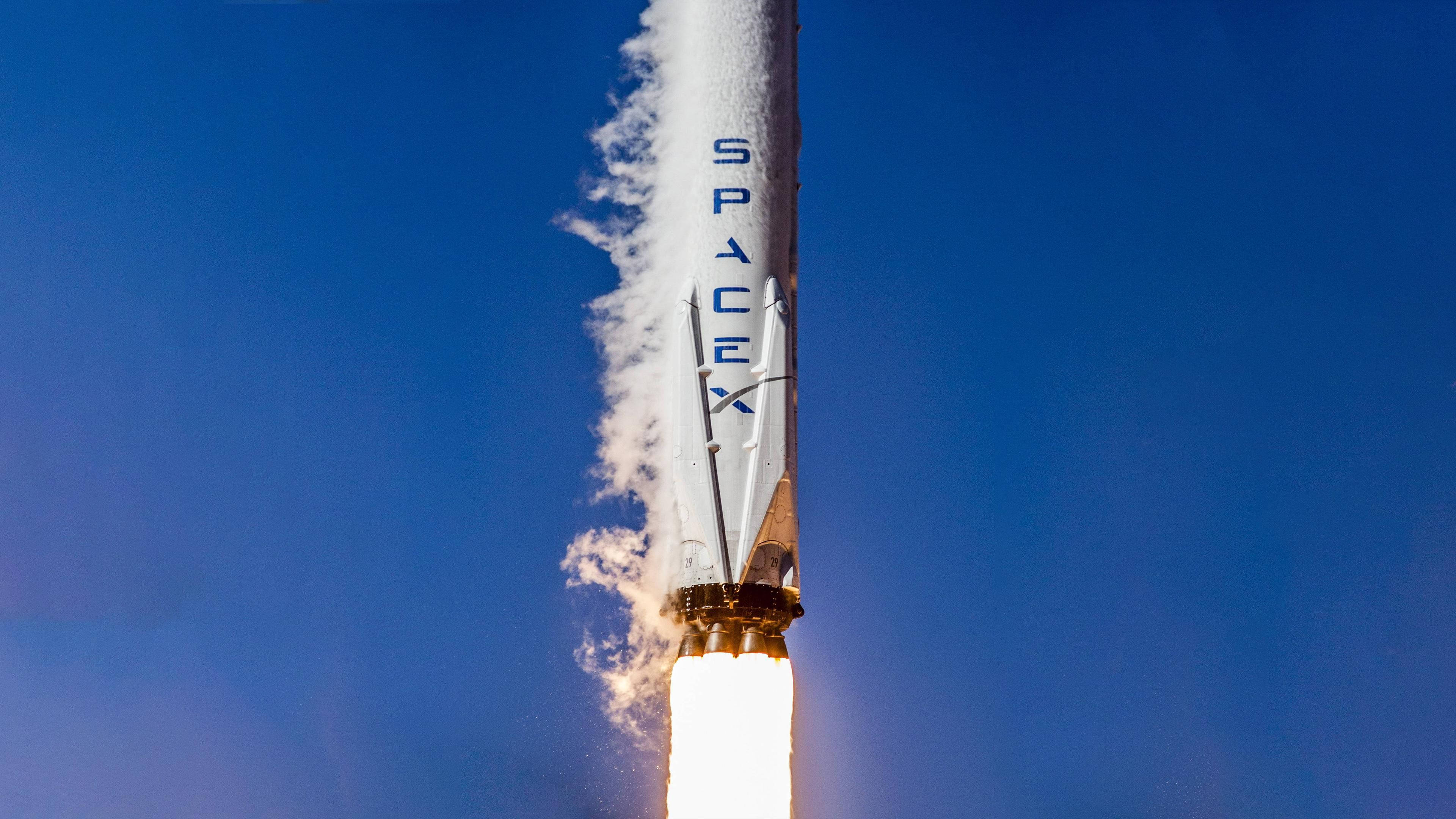 SpaceX 桌布 壁紙 — 一枚 SpaceX 火箭在晴朗的藍天下強力升空，下方拖著明亮熾熱的尾焰。