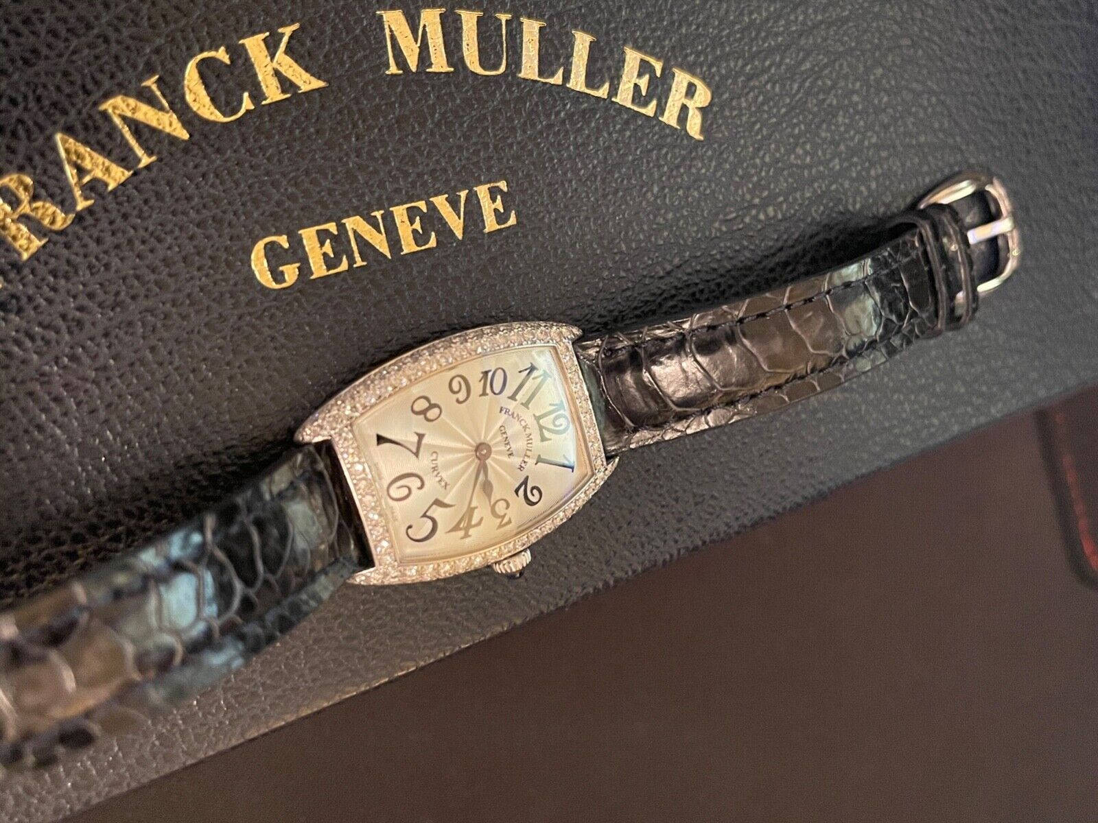 Black 桌布 壁紙 — 一枚Franck Muller Geneve腕錶，鑲鑽錶殼和鱷魚皮錶帶，優雅地放在其品牌皮革盒上。
