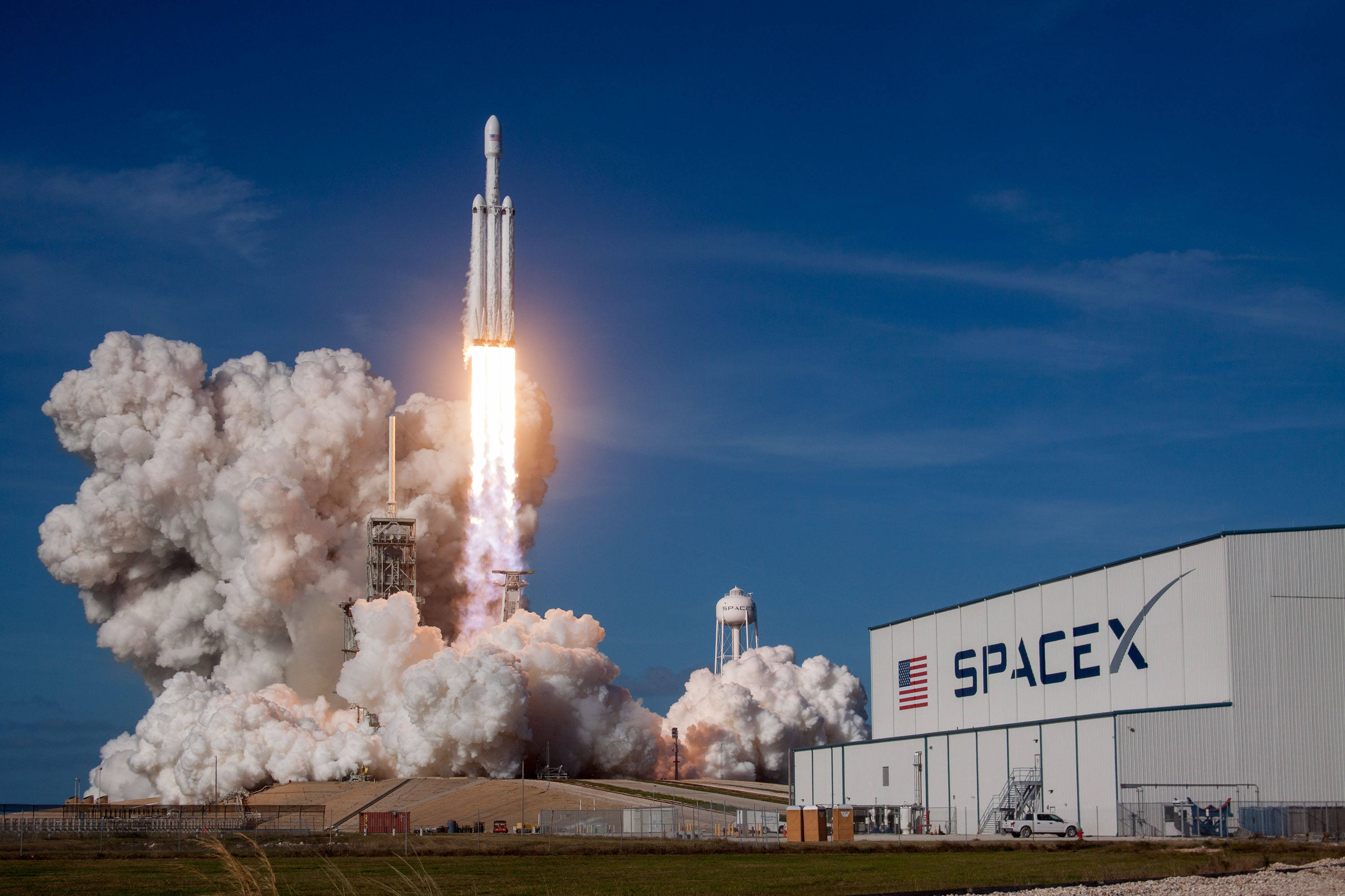 Starship 桌布 壁紙 — 一枚SpaceX火箭在晴朗藍天下從發射台升空，伴隨著熾熱的推力和滾滾濃煙。