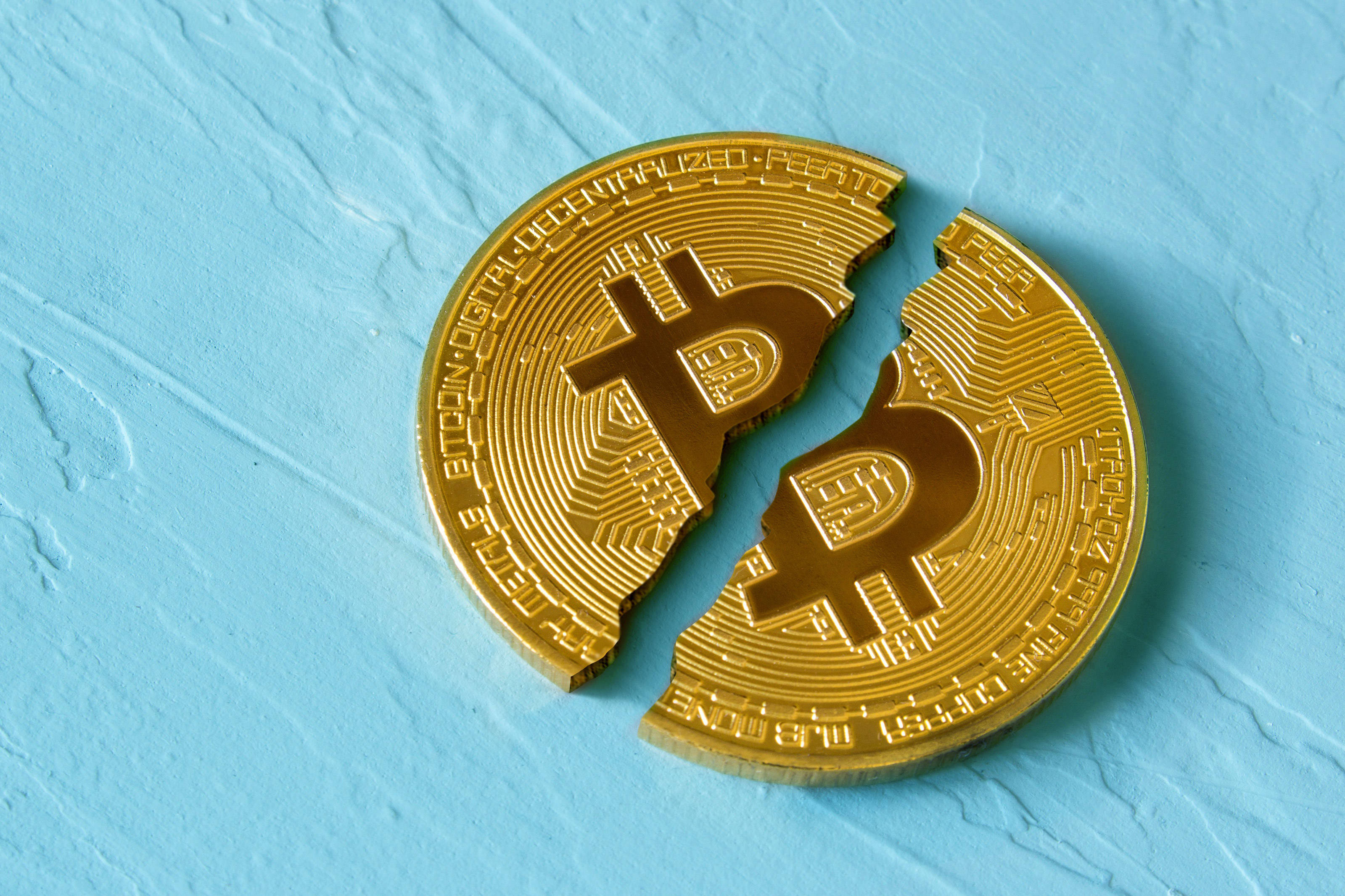Cryptocurrency 桌布 壁紙 — 一枚分成兩半的金色比特幣硬幣放在有紋理的淺藍色表面上。