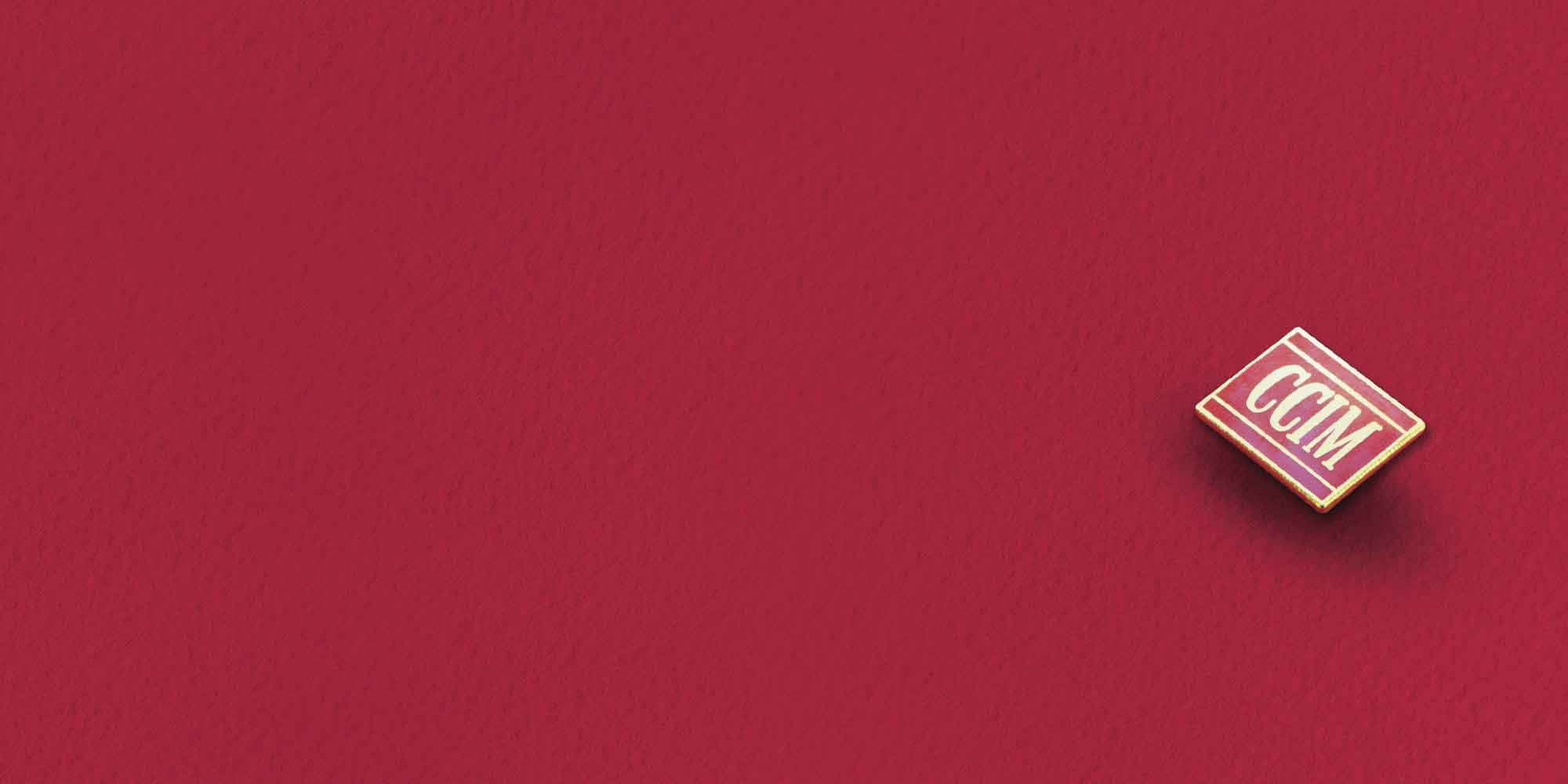 Fabric 桌布 壁紙 — 一枚帶有CCM字樣的細小紅金徽章，放置在帶有紋理的深紅色表面上。