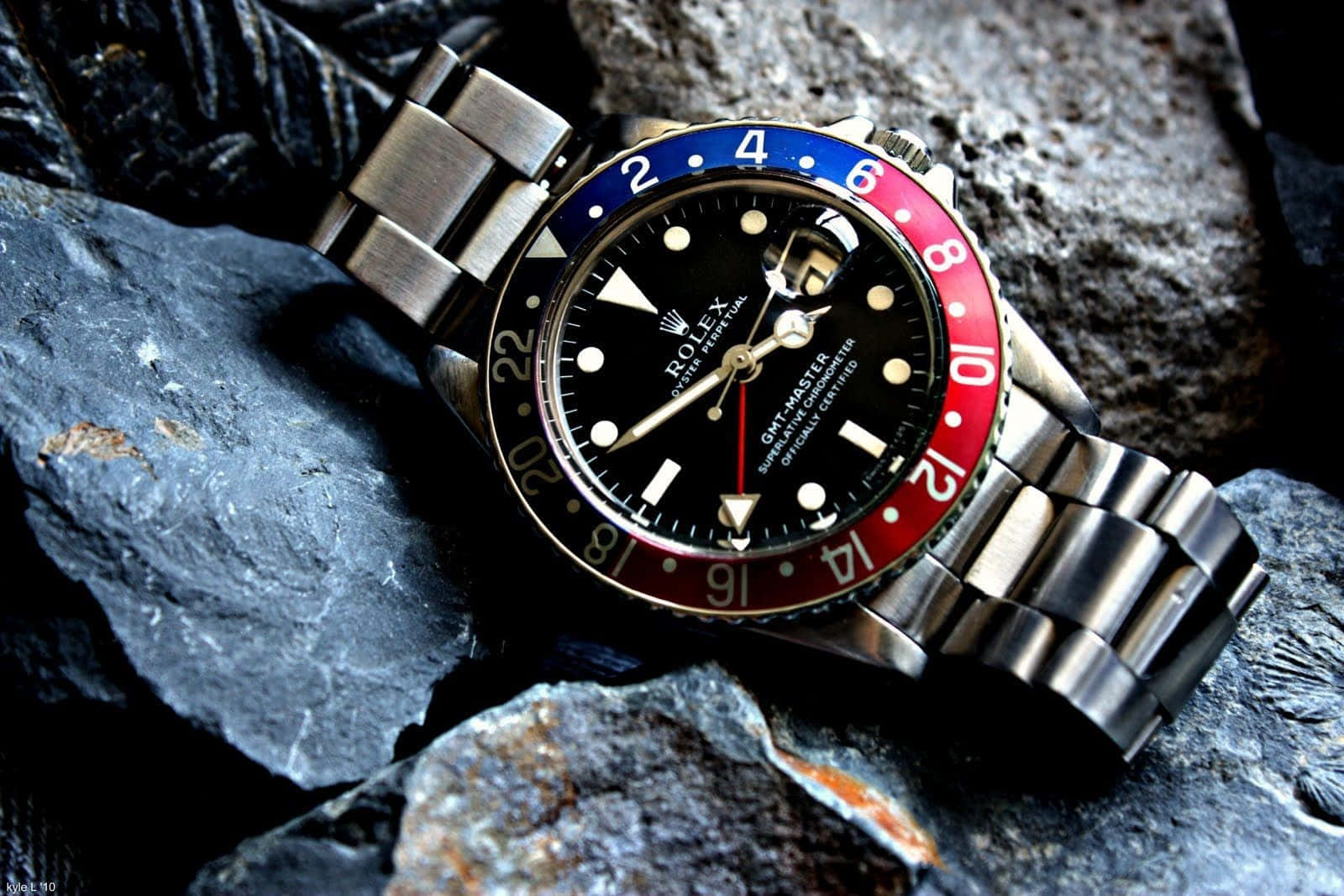 Rolex 桌布 壁紙 — 一枚帶有紅藍錶圈的勞力士GMT Master手錶，在明亮燈光下放置於深色紋理岩石上。
