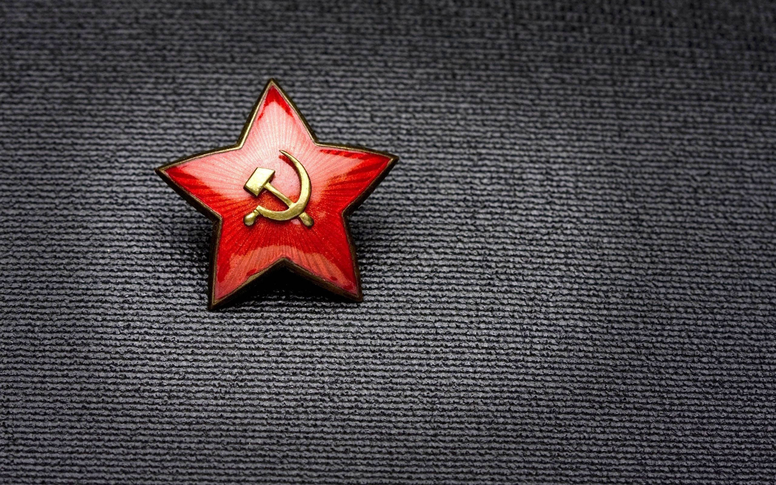 Red Star 桌布 壁紙 — 一枚帶有金色鎚子與鐮刀標誌的紅色星星別針，放在深色紋理布料表面上。