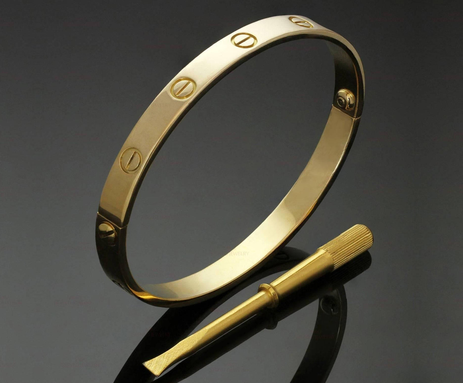 Ring 桌布 壁紙 — 一枚拋光金色Cartier love手鐲，帶有標誌性螺絲圖案，旁邊放著相配的金色螺絲刀，置於深色反光表面上。