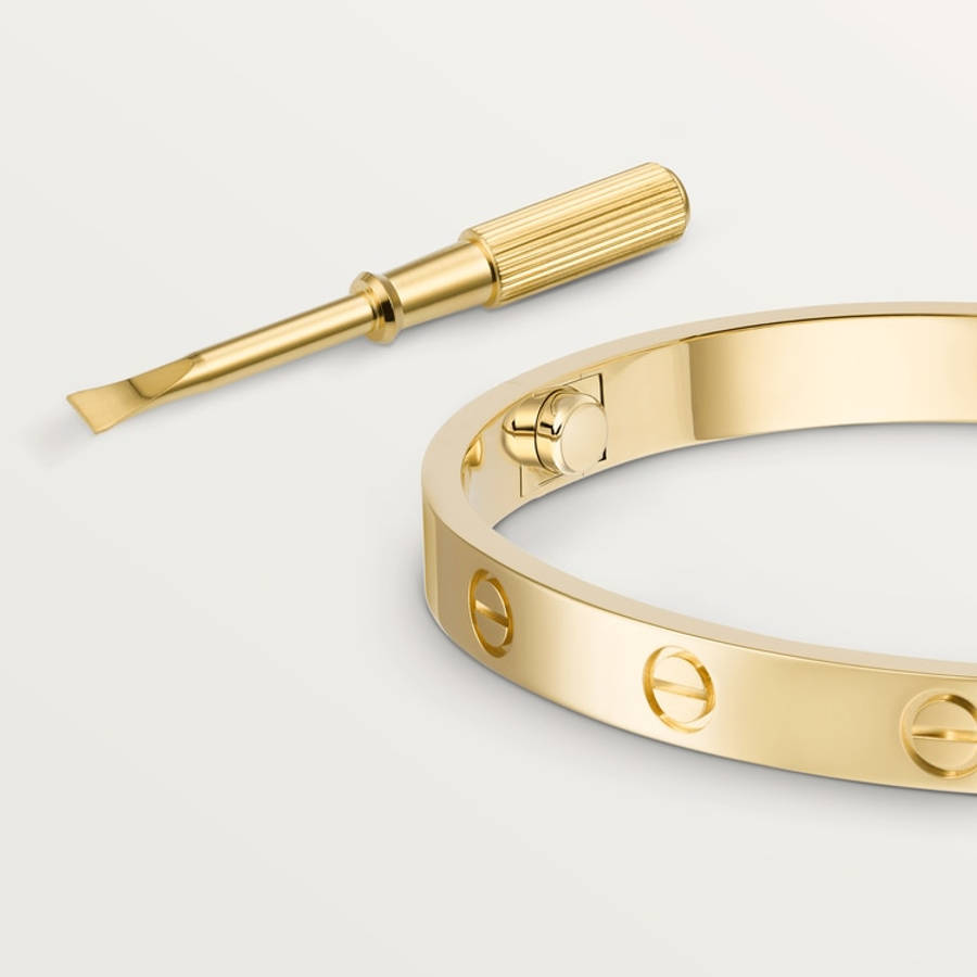 品牌 桌布 壁紙 — 一枚拋光金色Cartier LOVE手鐲，連同其標誌性螺絲和工具，優雅地放置在簡約的白色表面上。