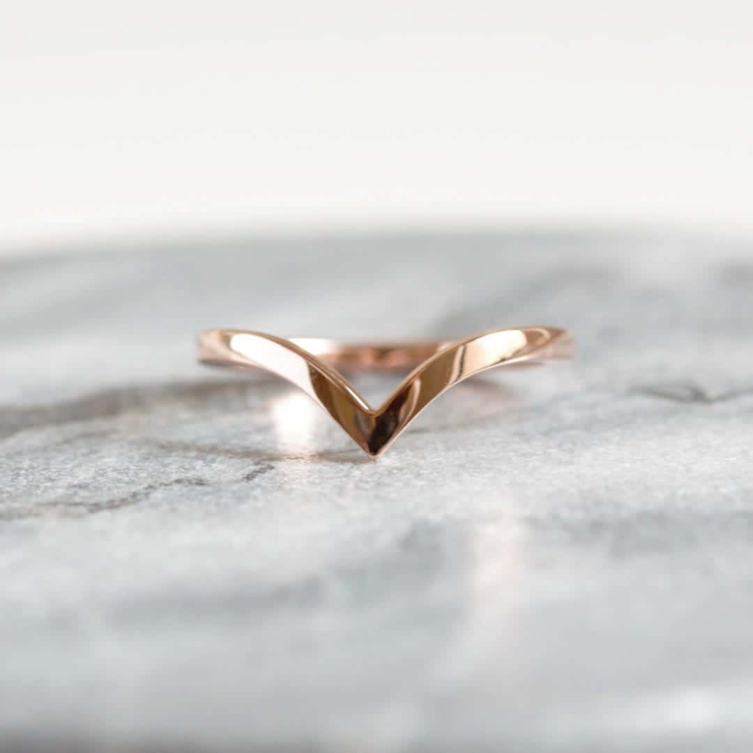 Wedding Rings 桌布 壁紙 — 一枚時尚的玫瑰金V形戒指，置於清涼的灰色大理石表面上，搭配柔和燈光。