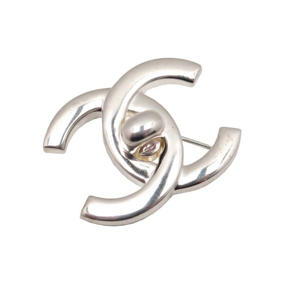 香奈兒標誌 桌布 壁紙 — 一枚時尚的銀色 Chanel CC 標誌胸針，帶有拋光曲線和中央金色點綴，背景為白色。