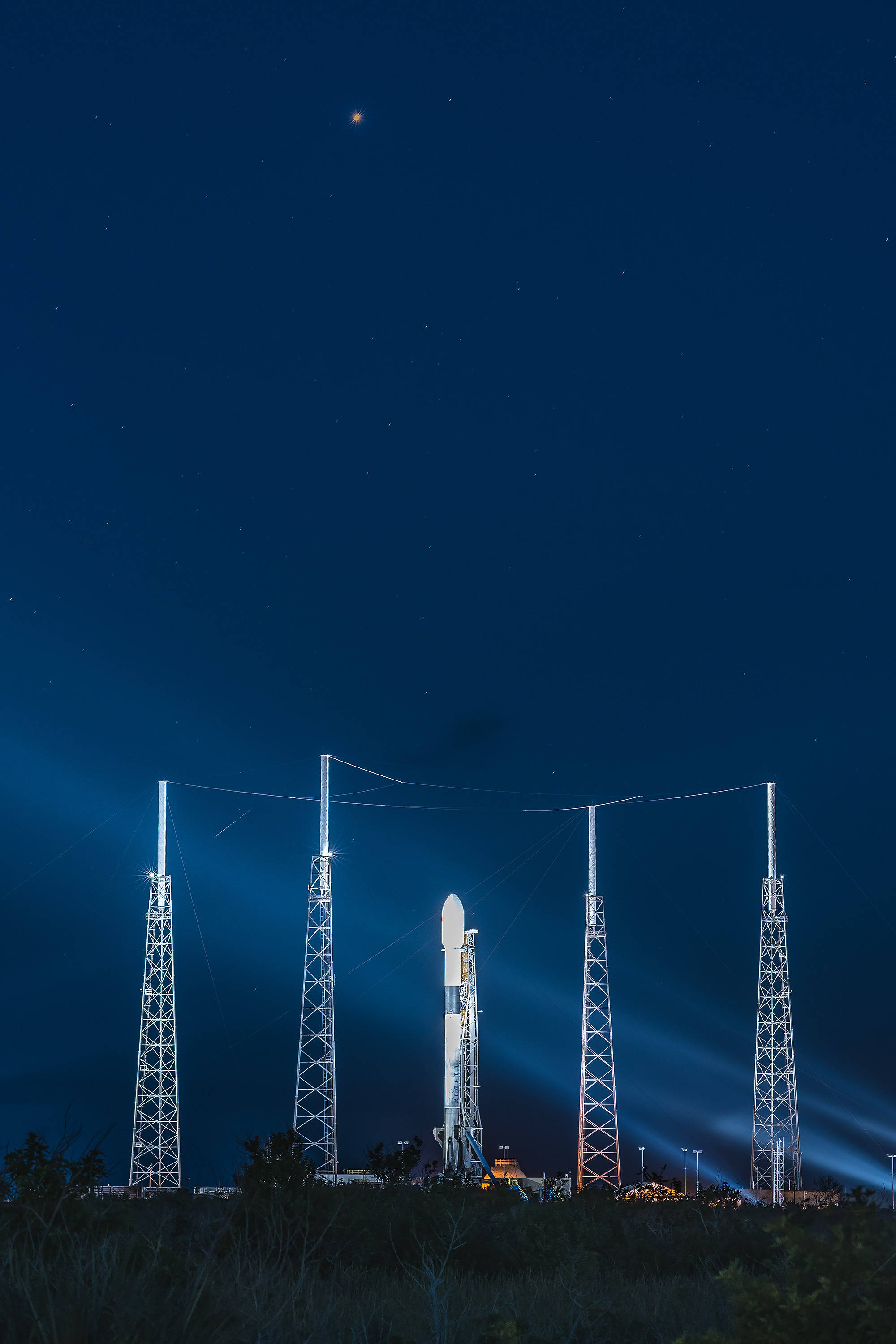 Aerospace 桌布 壁紙 — 一枚火箭在星光夜空下被聚光燈照亮，周圍是高聳的發射塔。