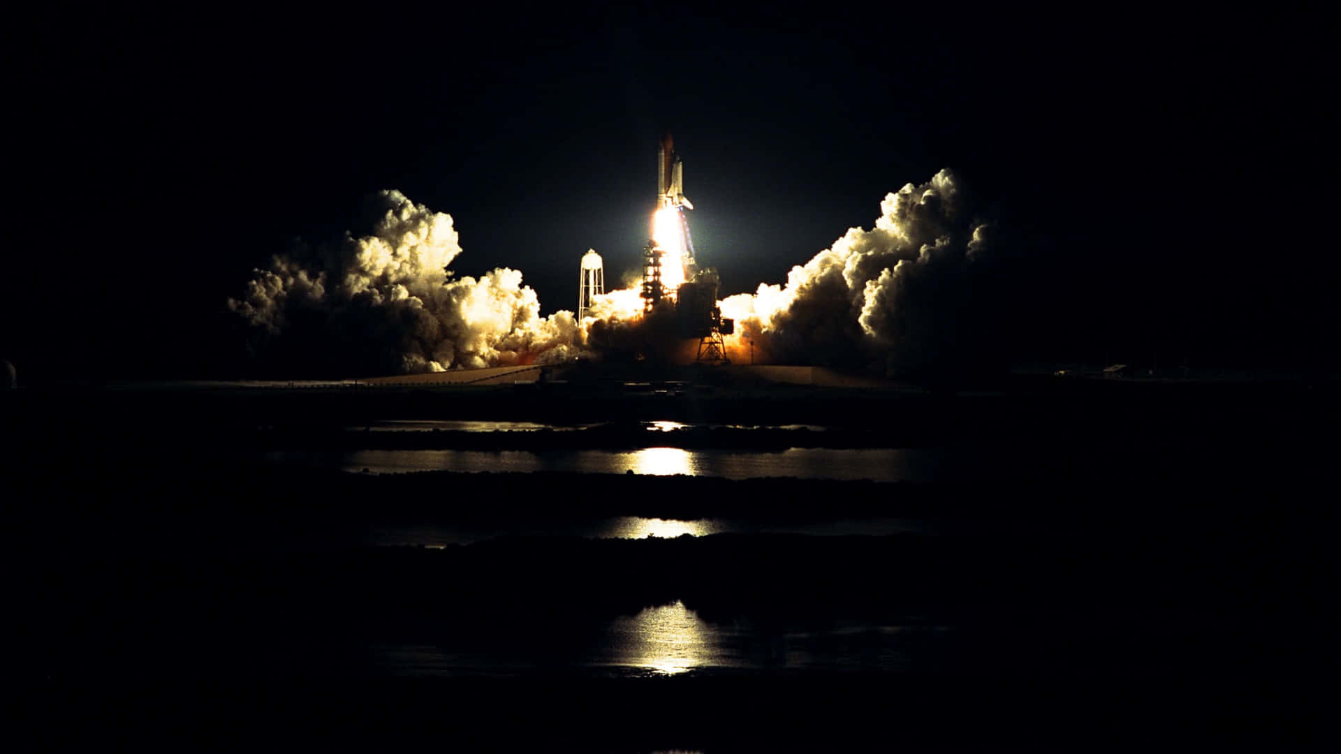 Space Mission 桌布 壁紙 — 一枚火箭在漆黑的夜空中點燃，噴射出熾熱的推力和滾滾濃煙，其倒影在下方平靜的水面上閃爍。