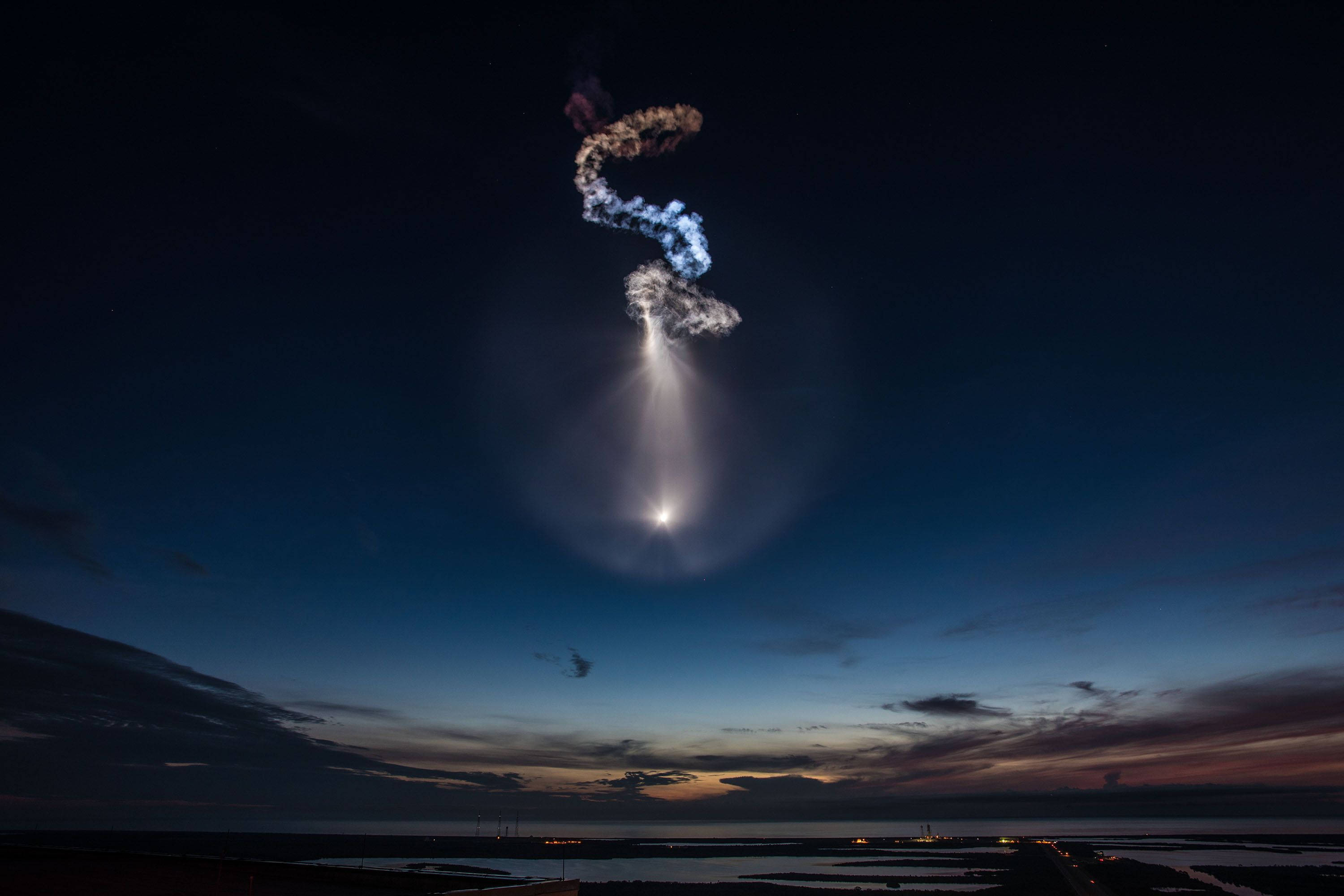 SpaceX 桌布 壁紙 — 一枚火箭在黃昏時升空，在深藍色的暮色天空中留下發光的軌跡和煙霧螺旋。