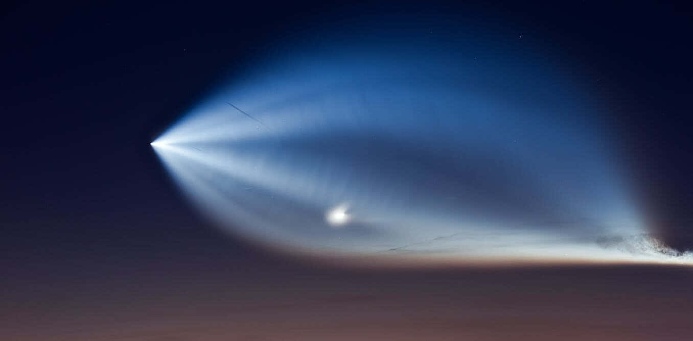 外星人 桌布 壁紙 — 一枚火箭發射到夜空，在黑暗的星空背景下留下明亮的藍色離子軌跡。