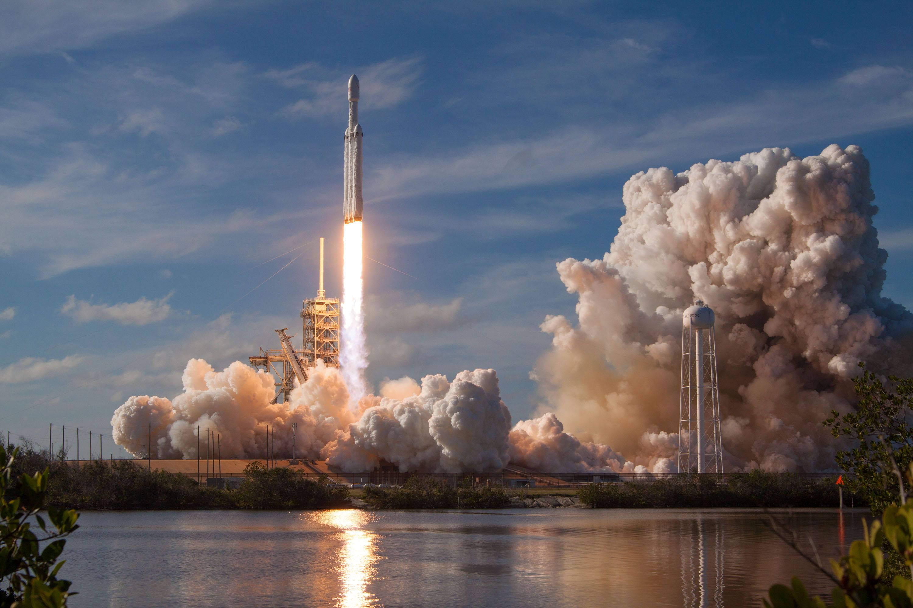 SpaceX 桌布 壁紙 — 一枚火箭發射到藍天，在平靜的水道上留下熾熱的軌跡和滾滾濃煙。
