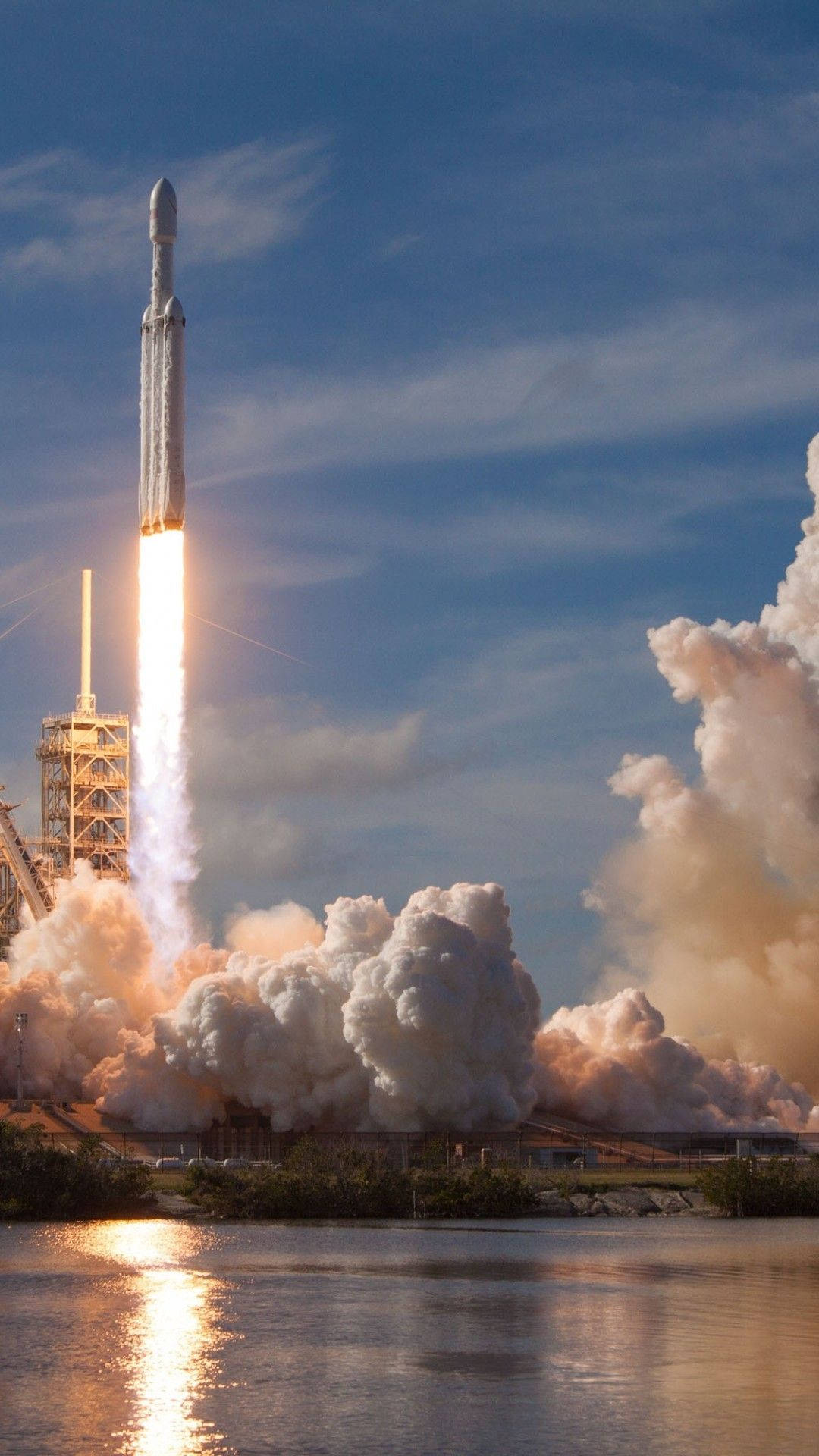 SpaceX 桌布 壁紙 — 一枚火箭衝上晴朗藍天，在平靜水面上留下熾熱軌跡和滾滾濃煙。