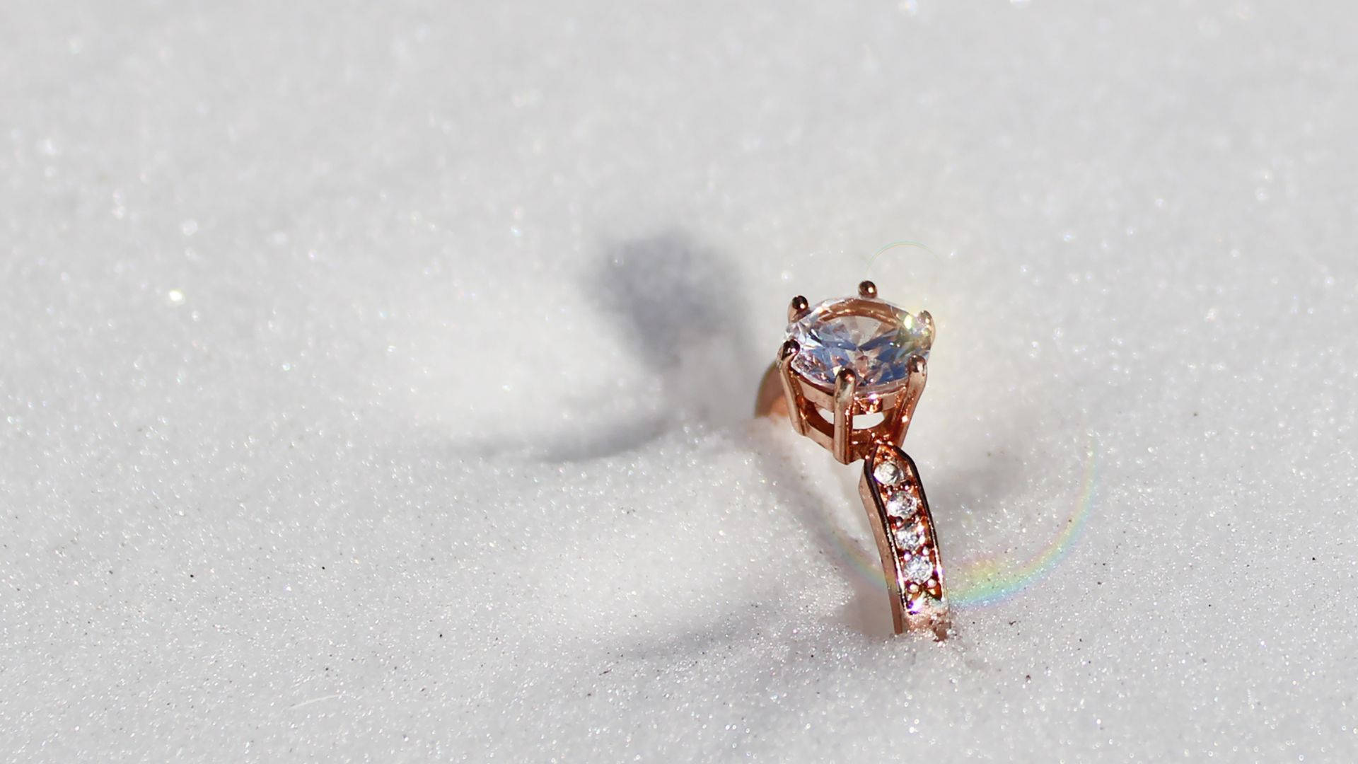 Diamond 桌布 壁紙 — 一枚玫瑰金訂婚戒指，鑲有大型藍色寶石和鑽石點綴，部分埋藏在純淨的白雪中。