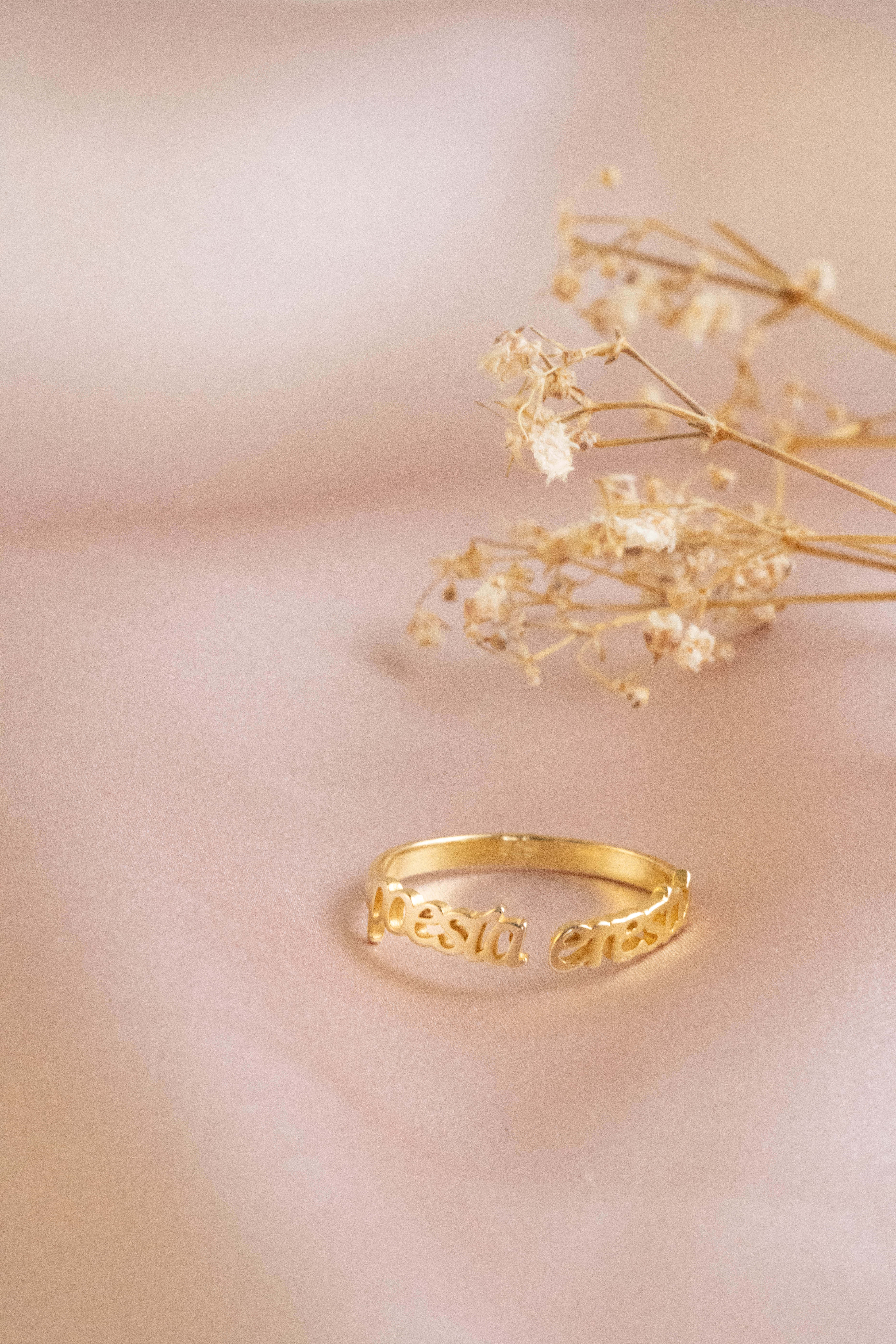 Gold Jewellery 桌布 壁紙 — 一枚精緻的金戒指上刻有文字，旁邊放著乾燥的滿天星，置於柔軟的粉紅色表面上。