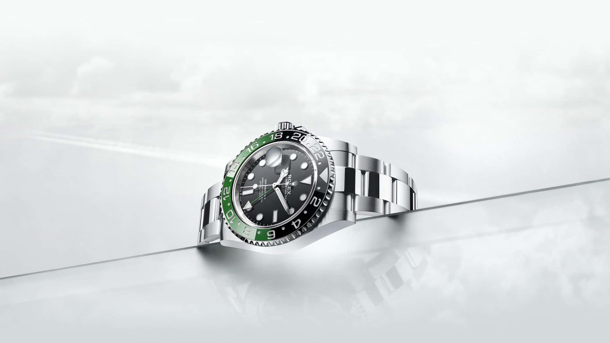 Rolex 桌布 壁紙 — 一枚綠色錶圈的勞力士GMT-Master II腕錶，在柔和的工作室燈光下，優雅地放置在光滑的白色反光表面上。