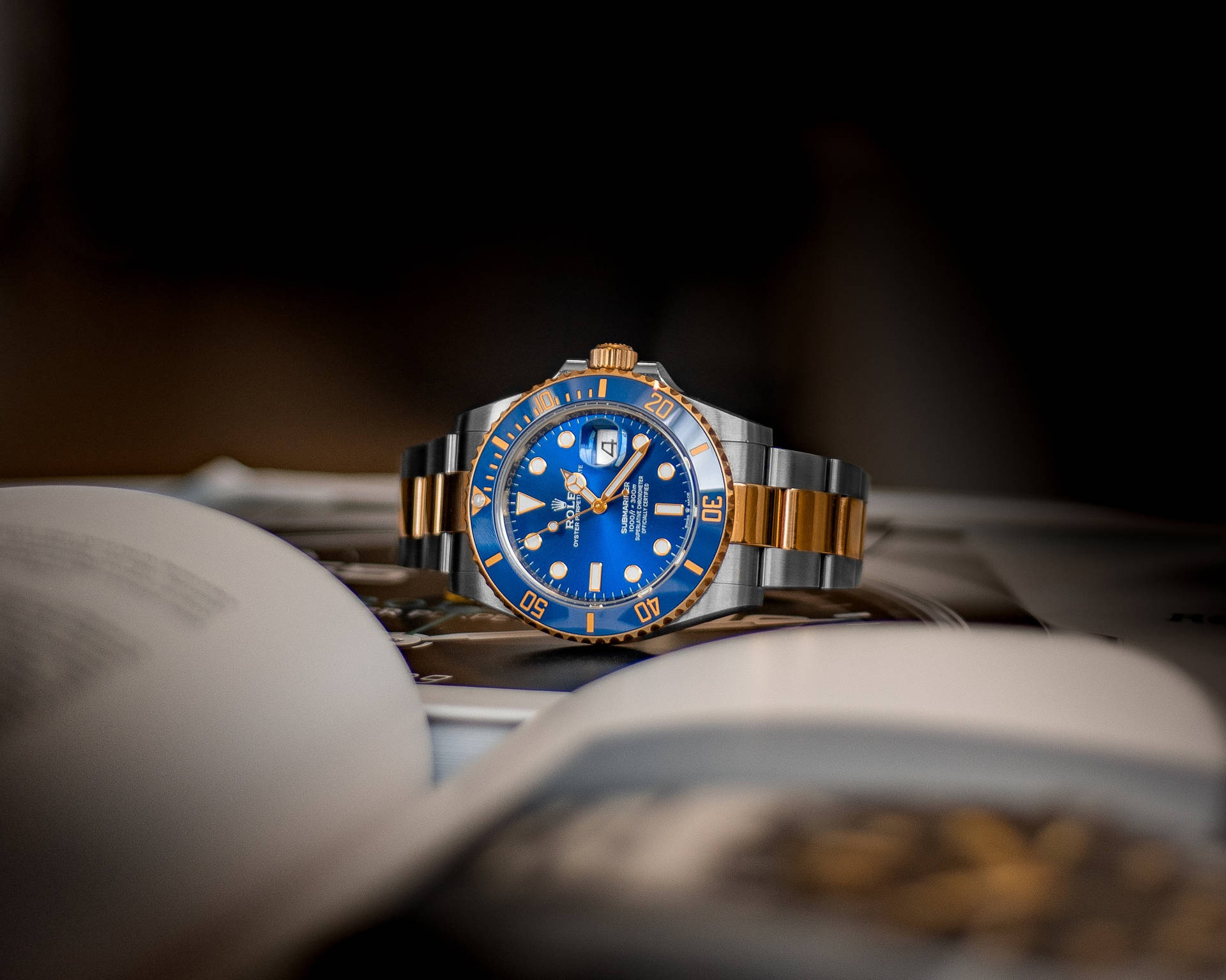 Vintage 桌布 壁紙 — 一枚豪華的勞力士Submariner，藍色錶盤配金色點綴，優雅地擱在一本打開的書上，在柔和的工作室燈光下。
