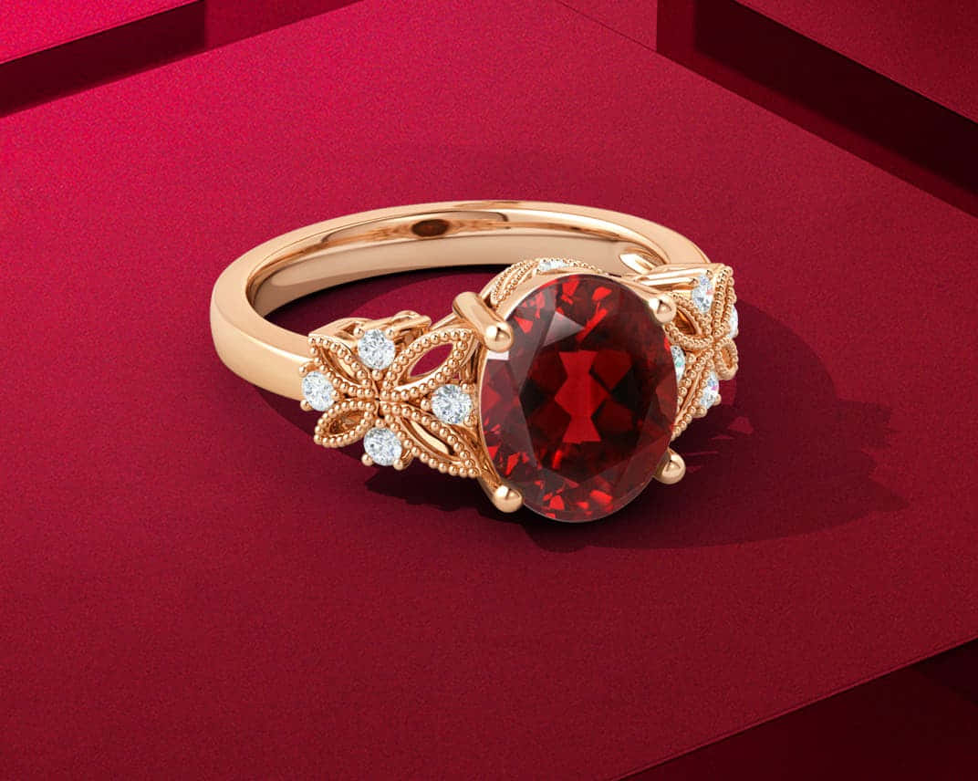 Red Diamond 桌布 壁紙 — 一枚金戒指，鑲有大型紅色寶石和鑽石點綴，在工作室燈光下放置於濃郁的紅色表面上。