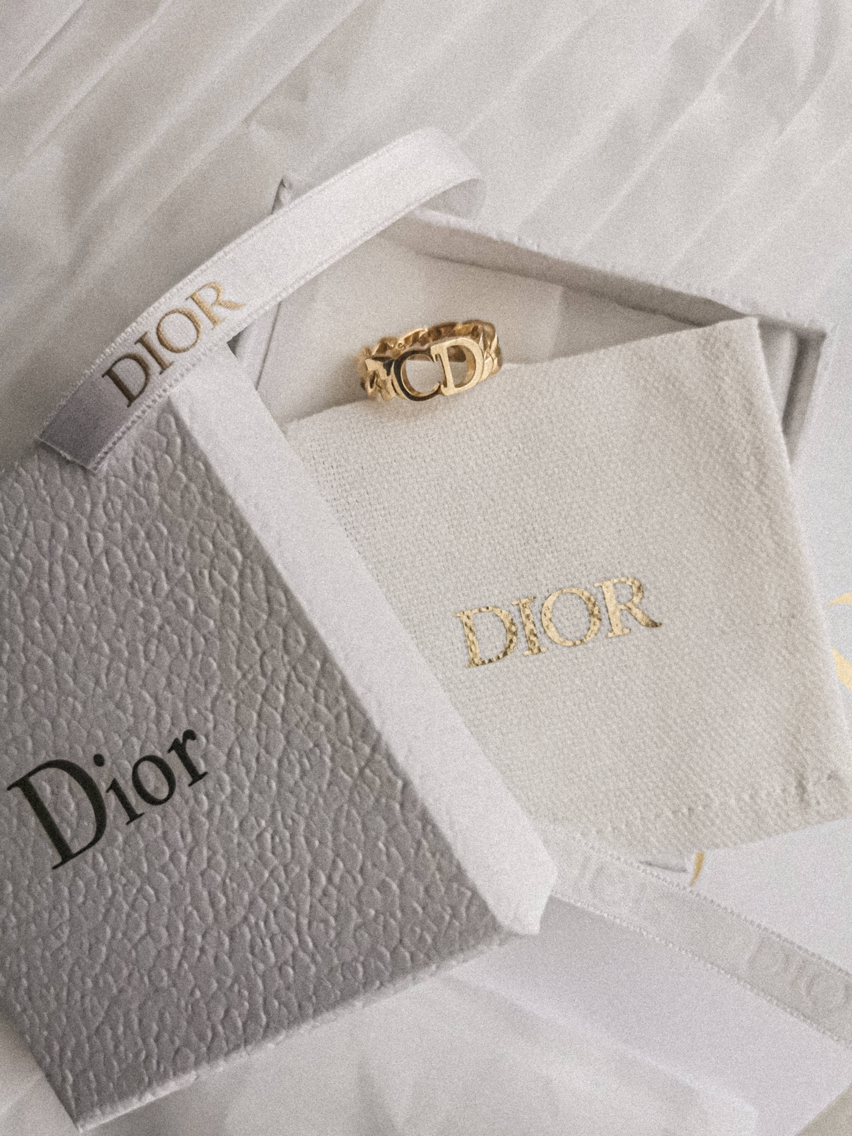 Dior 動態 桌布 壁紙 — 一枚金色Dior戒指優雅地放置在襯有白色布料和絲帶的品牌盒子中。