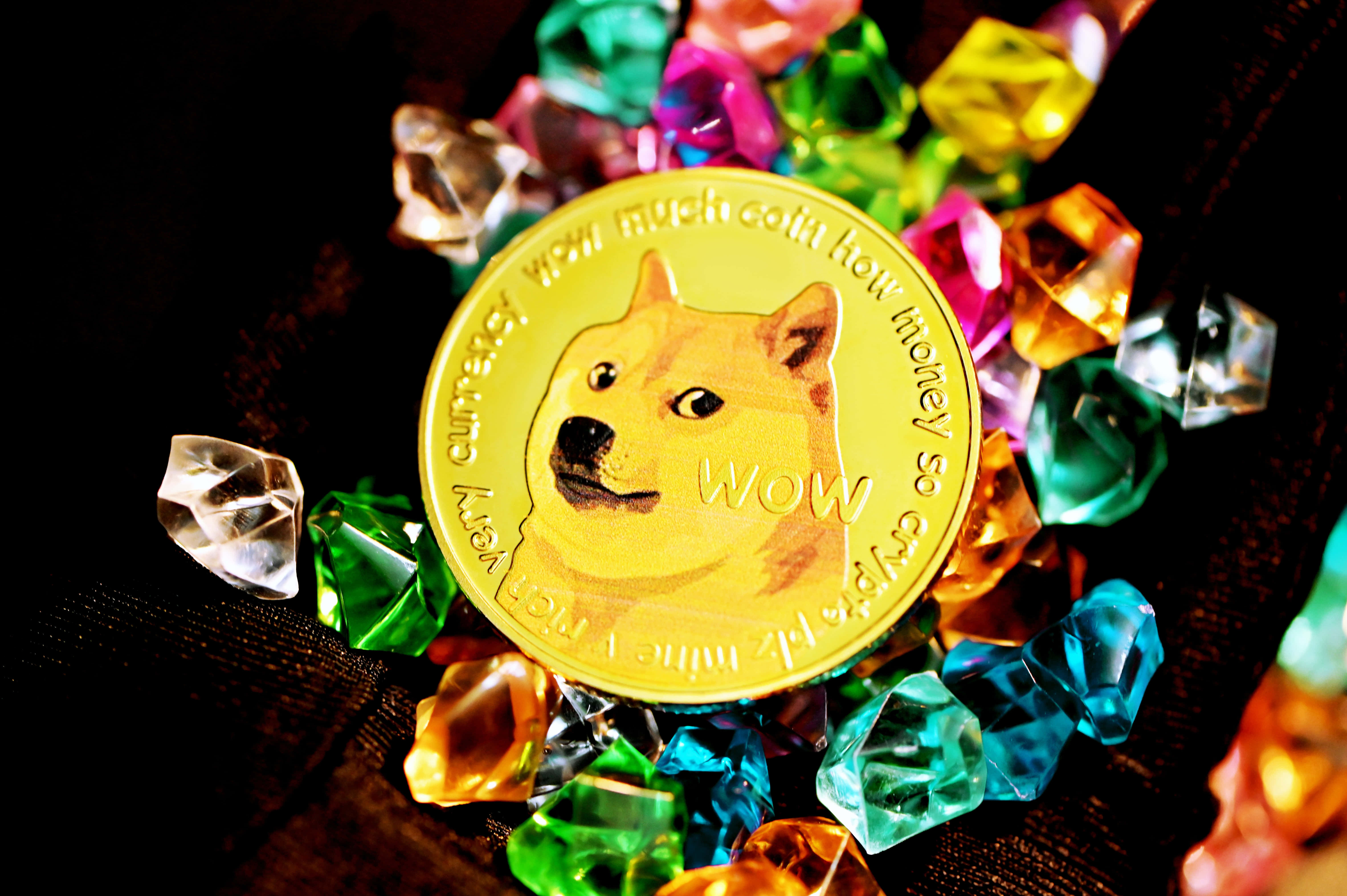Dogecoin 桌布 壁紙 — 一枚金色Dogecoin，上面有柴犬圖案，放置在深色紋理表面上，周圍是色彩繽紛的切割寶石。