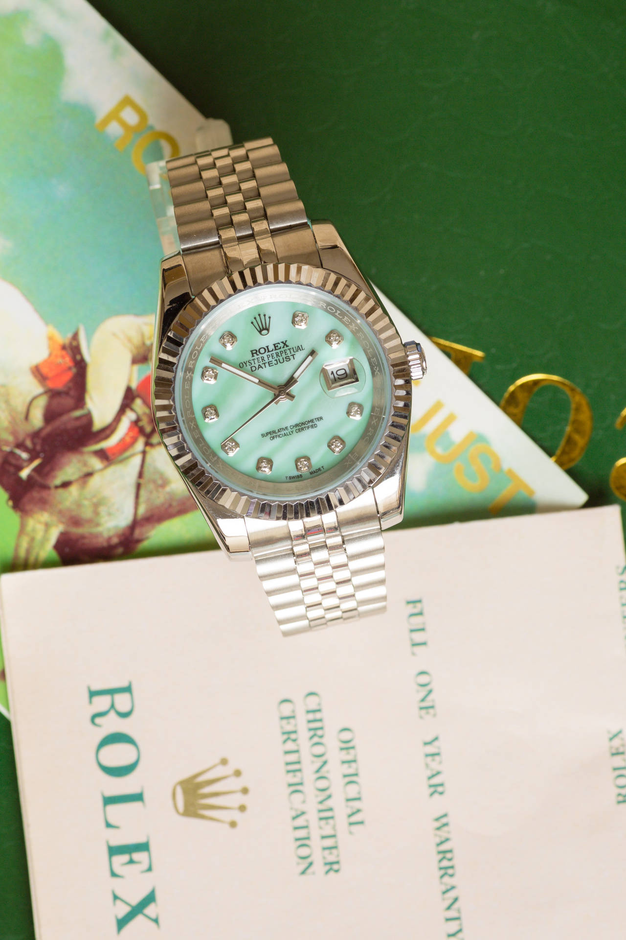 Designer Logo 桌布 壁紙 — 一枚銀色勞力士Oyster Perpetual，配備鑽石時標和薄荷綠色錶盤，放置在官方勞力士保固和認證文件上。