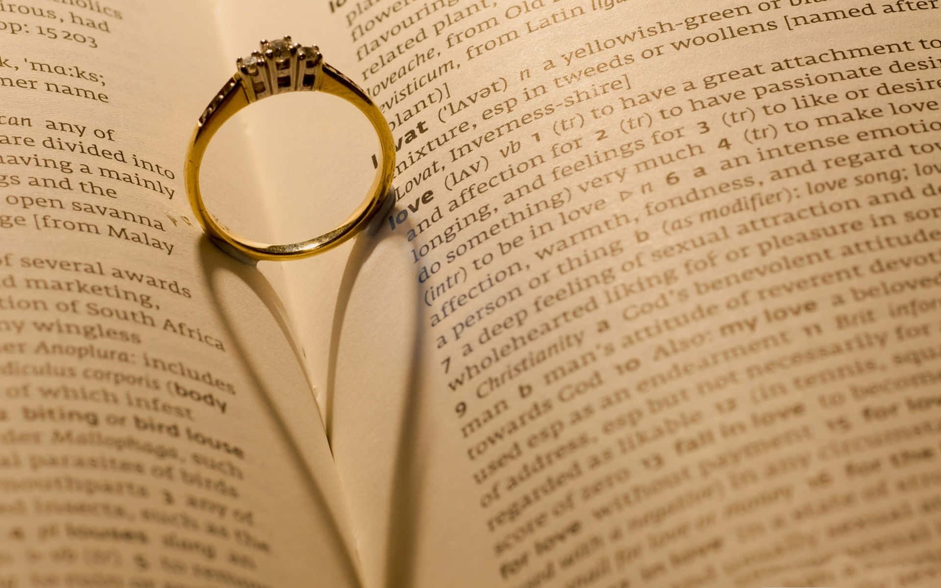 rings 桌布 壁紙 — 一枚鑲有鑽石的金色訂婚戒指放在一本打開的字典頁面上，該頁面定義了「愛」這個詞。