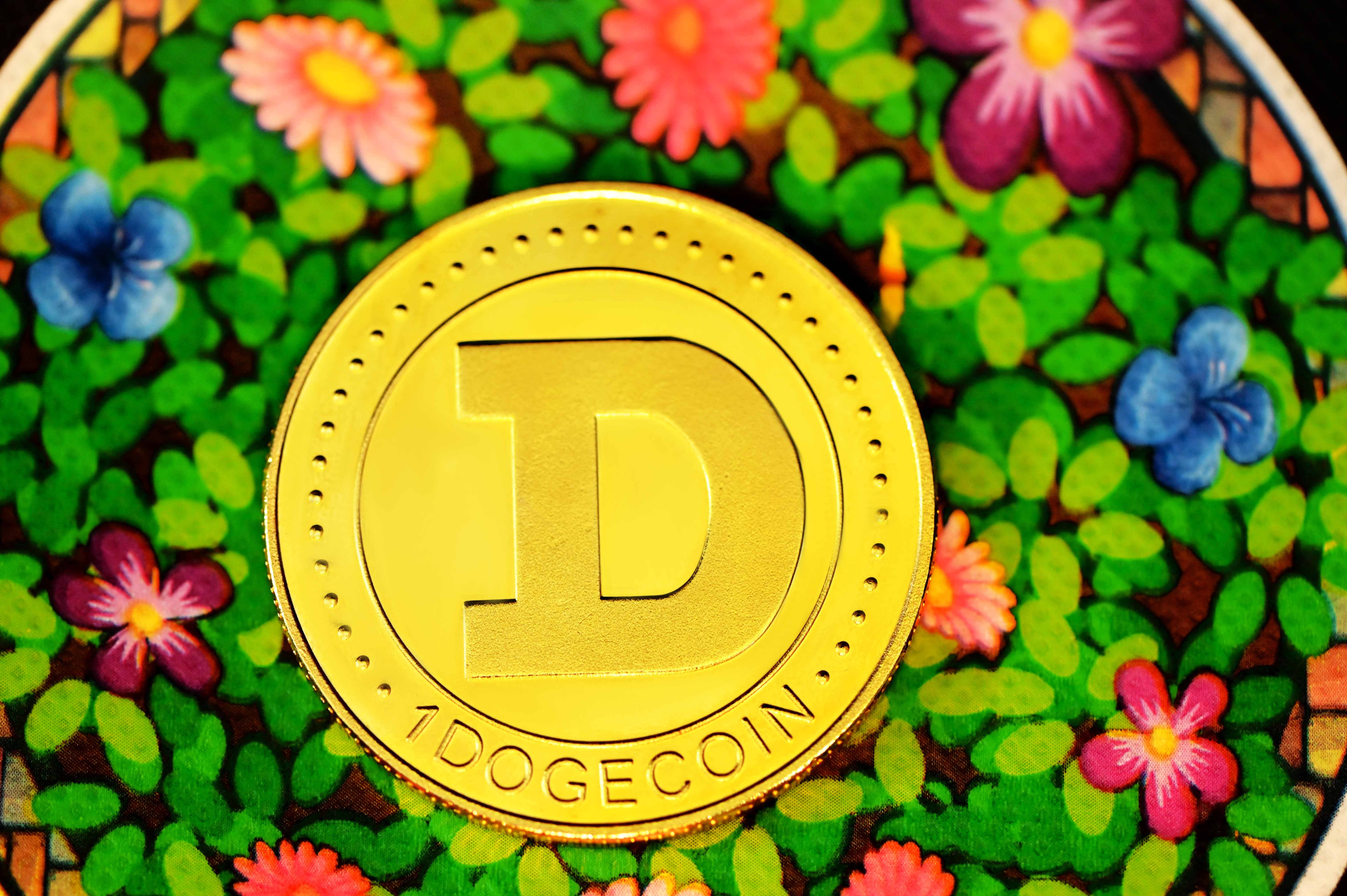 Dogecoin 桌布 壁紙 — 一枚閃亮的金色狗狗幣放在色彩繽紛的花卉圖案表面上，有鮮豔的粉紅色、藍色和紫色花朵。