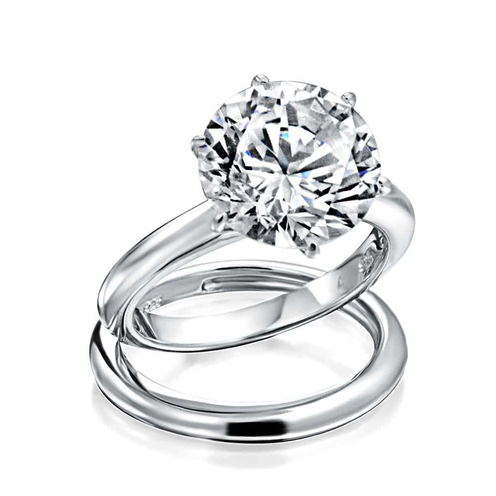 Wedding Ring 桌布 壁紙 — 一枚閃亮的銀色訂婚戒指，鑲有一顆大圓形鑽石，置於相配的結婚戒指之上，兩者交織在純白背景前。