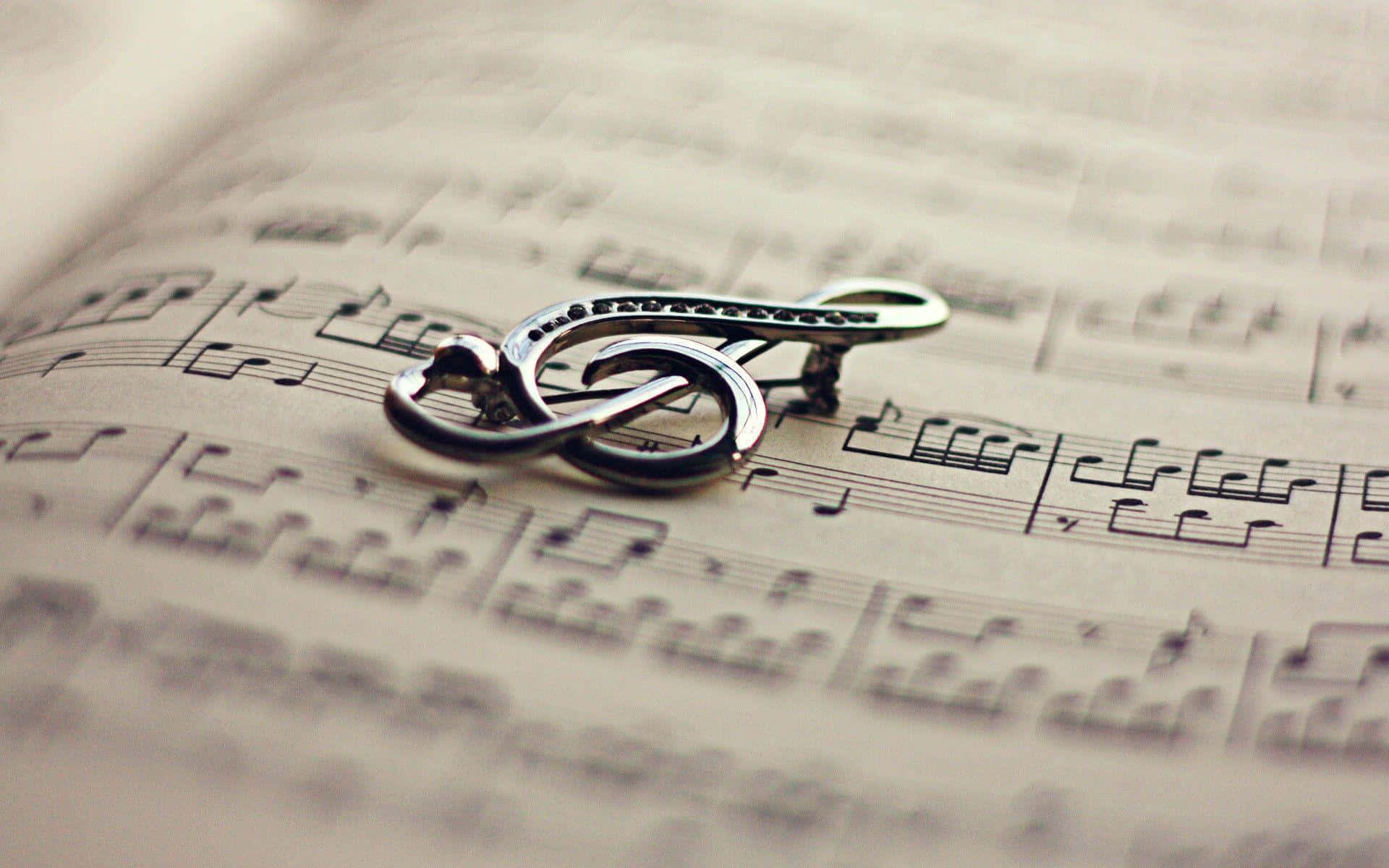 Music Notes 桌布 壁紙 — 一枚閃亮的銀色高音譜號胸針優雅地放在泛黃的樂譜上，樂譜上的音符以柔焦模糊處理。