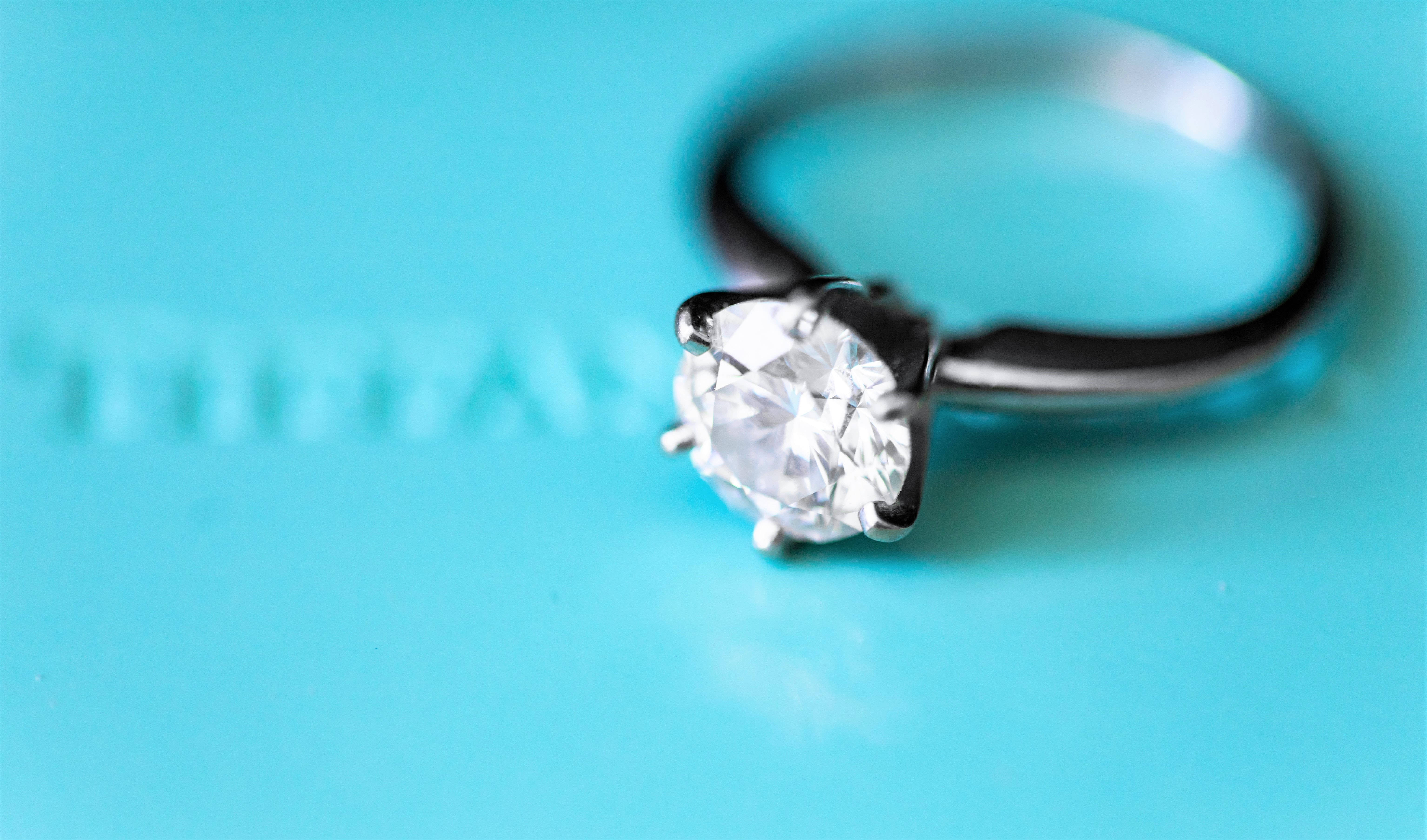 tiffany 桌布 壁紙 — 一枚閃爍的鑽石單石戒指在鮮藍色Tiffany盒子上閃耀，品牌標誌模糊。