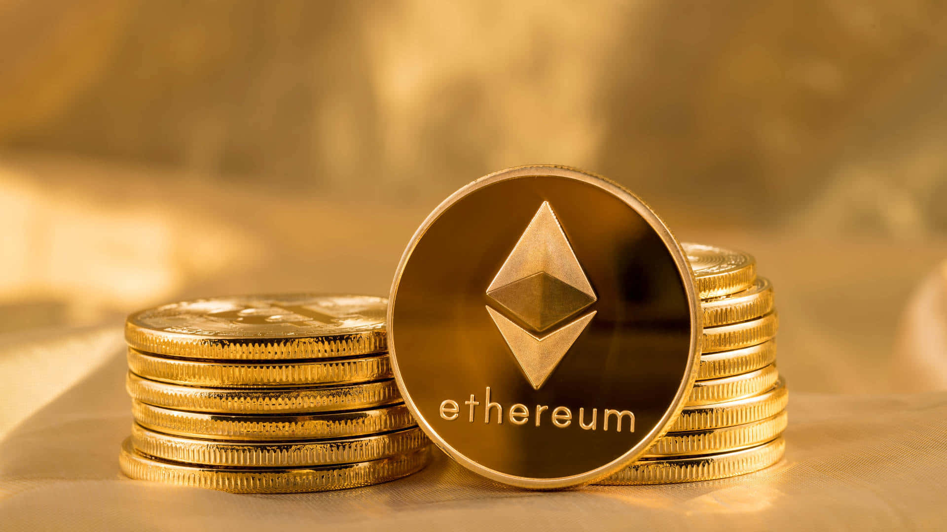 金錢 桌布 壁紙 — 一枚閃閃發光的金色以太幣直立在一堆類似硬幣旁邊，沐浴在溫暖的金色光線下。