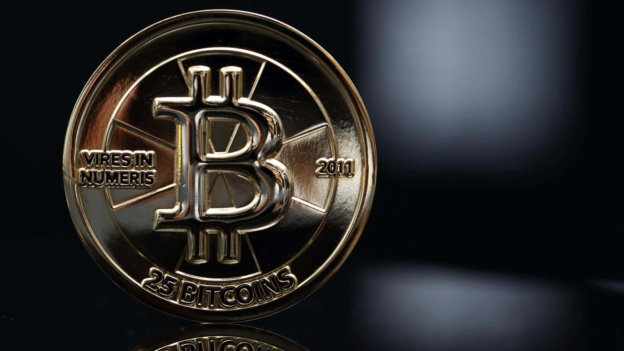 4K Bitcoin 桌布 壁紙 — 一枚閃閃發光的金色比特幣硬幣，上面刻有「25 BITCOINS」和「2011」，置於模糊的深色背景上。