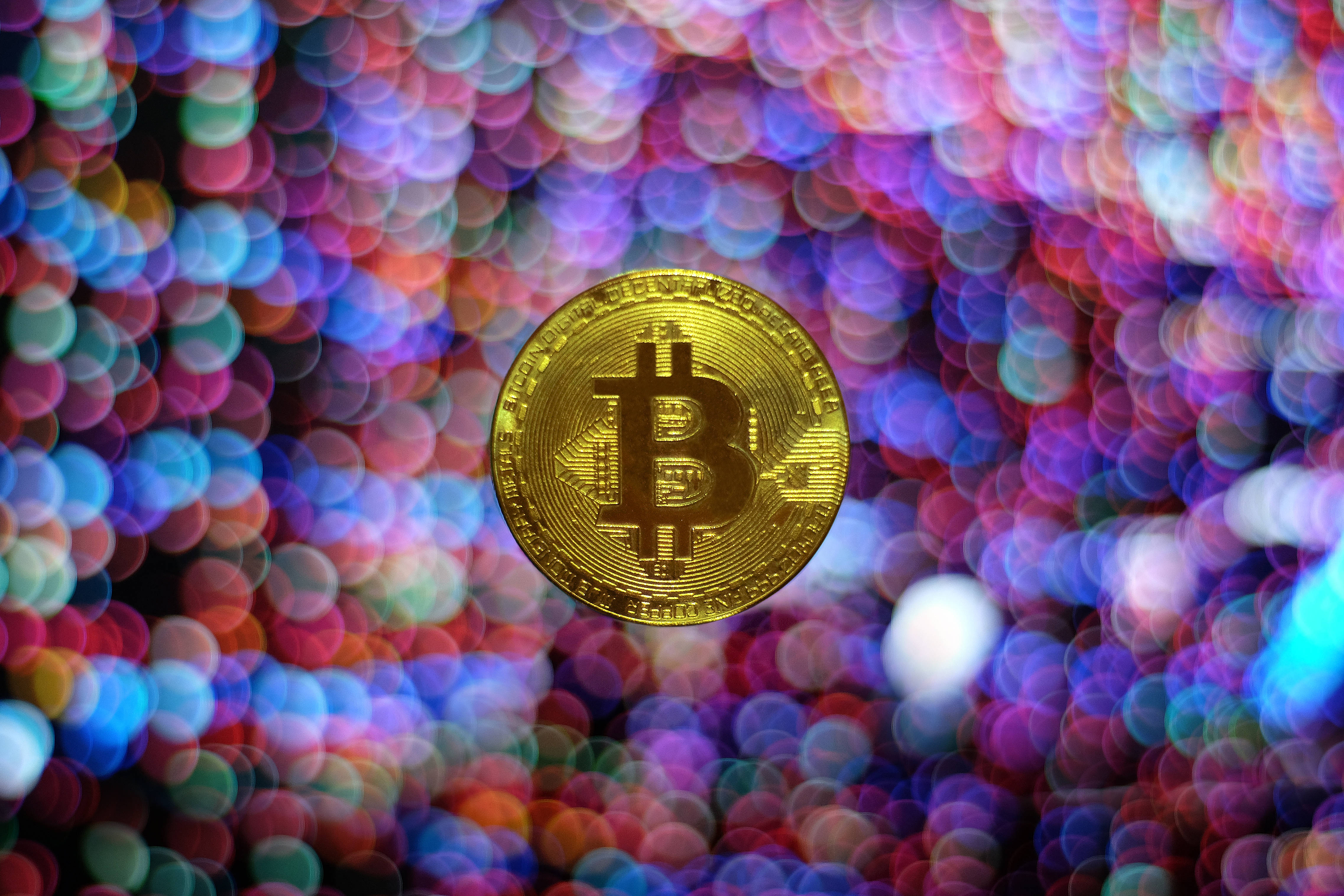 比特幣 桌布 壁紙 — 一枚閃閃發光的金色比特幣硬幣，以多彩燈光的鮮豔散景背景為中心。