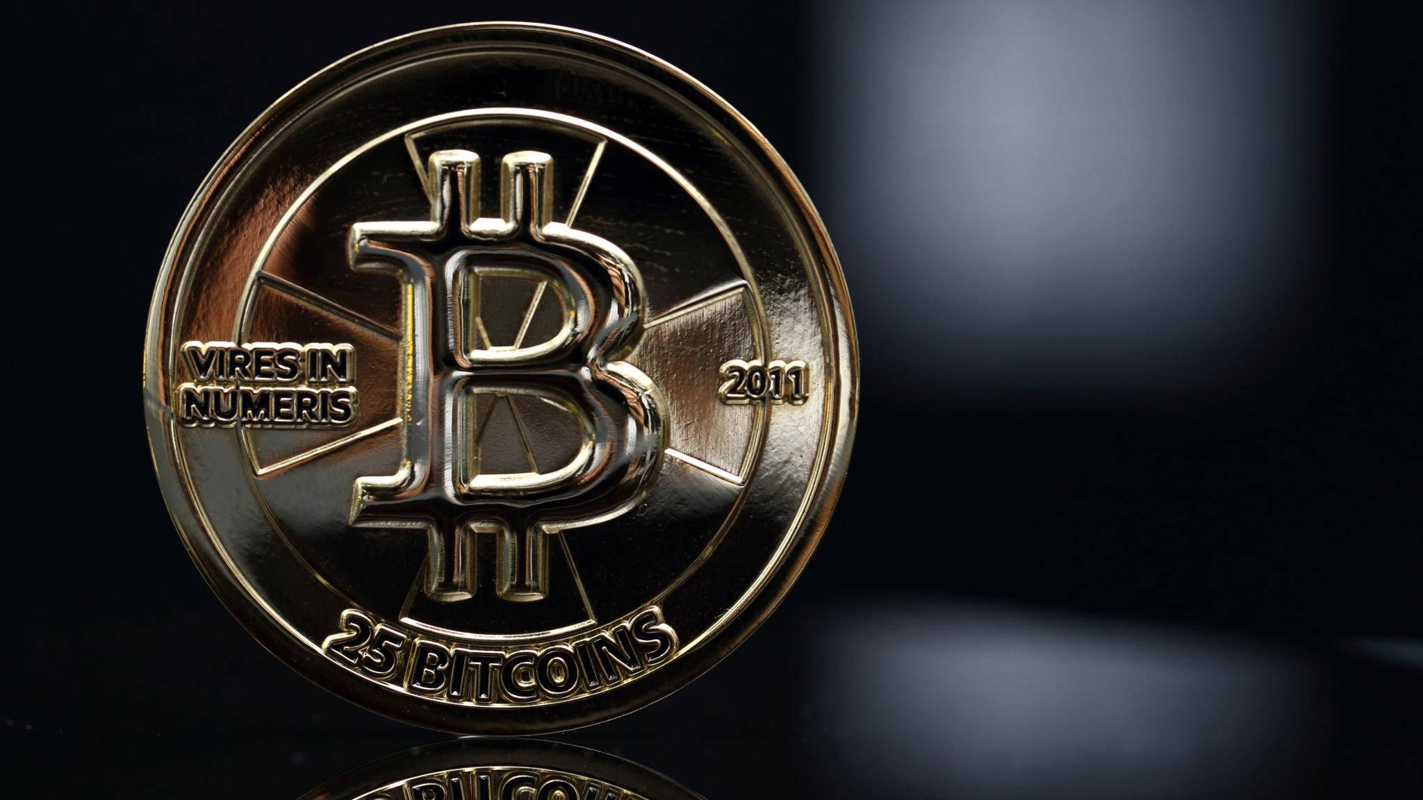 比特幣 桌布 壁紙 — 一枚閃閃發光的金色比特幣硬幣，刻有「25 BITCOINS」和「2011」，置於黑暗模糊的背景上。