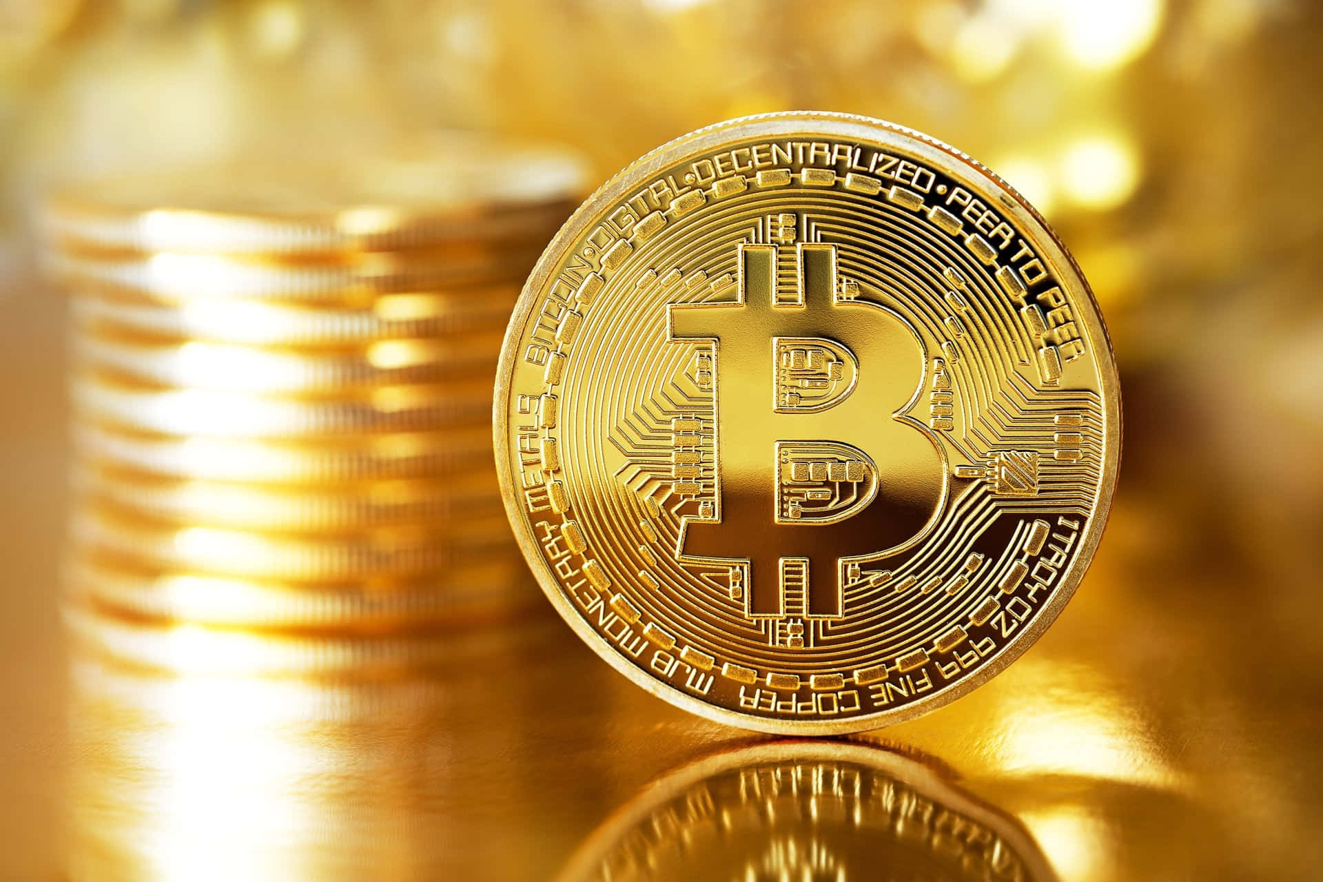 比特幣 桌布 壁紙 — 一枚閃閃發光的金色比特幣硬幣，清晰對焦，背後有一堆模糊的同類硬幣，全部沐浴在溫暖的金色光芒中。