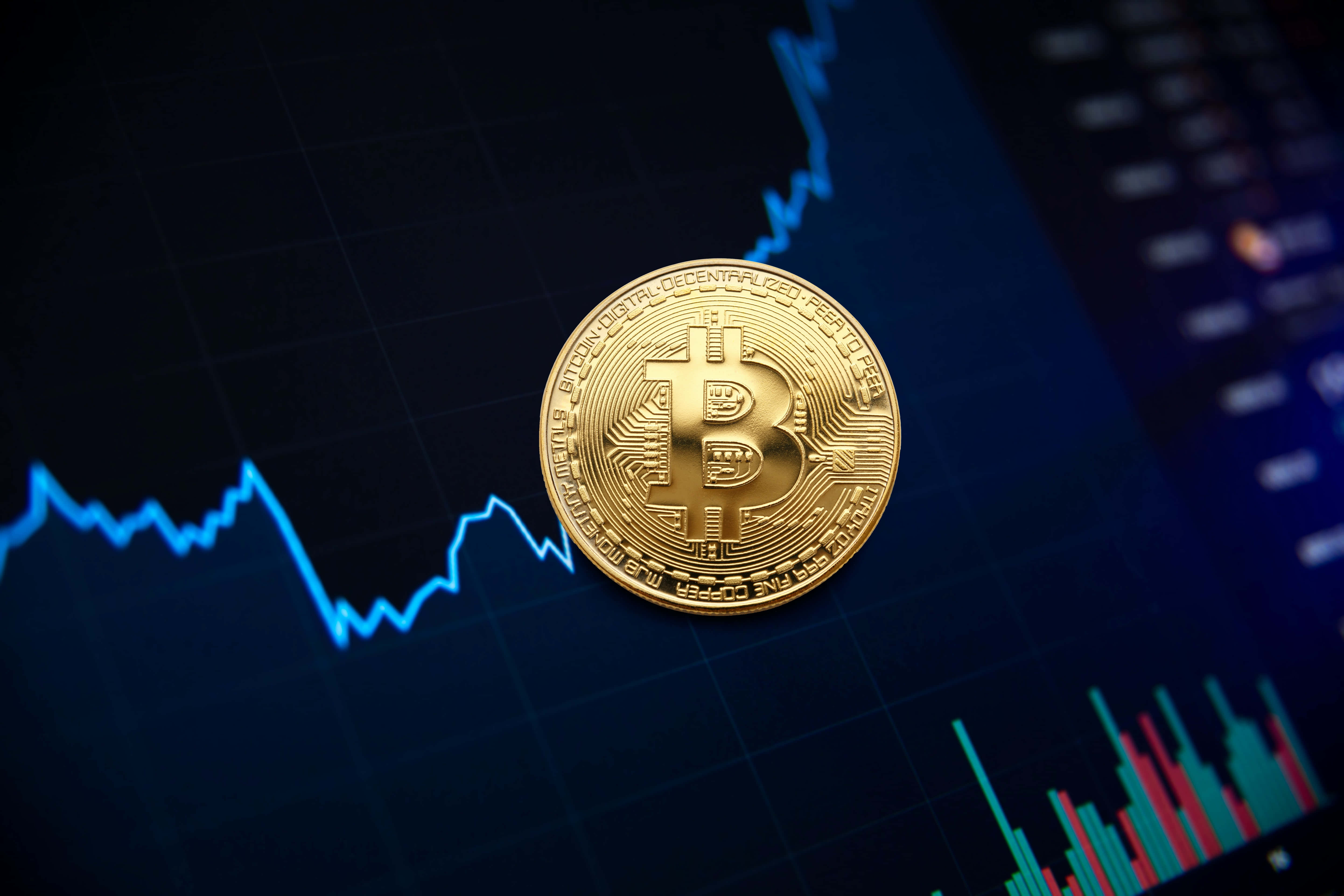 Mining 桌布 壁紙 — 一枚閃閃發光的金色比特幣硬幣放在一個顯示波動的藍色和紅色金融圖表的黑色螢幕上。