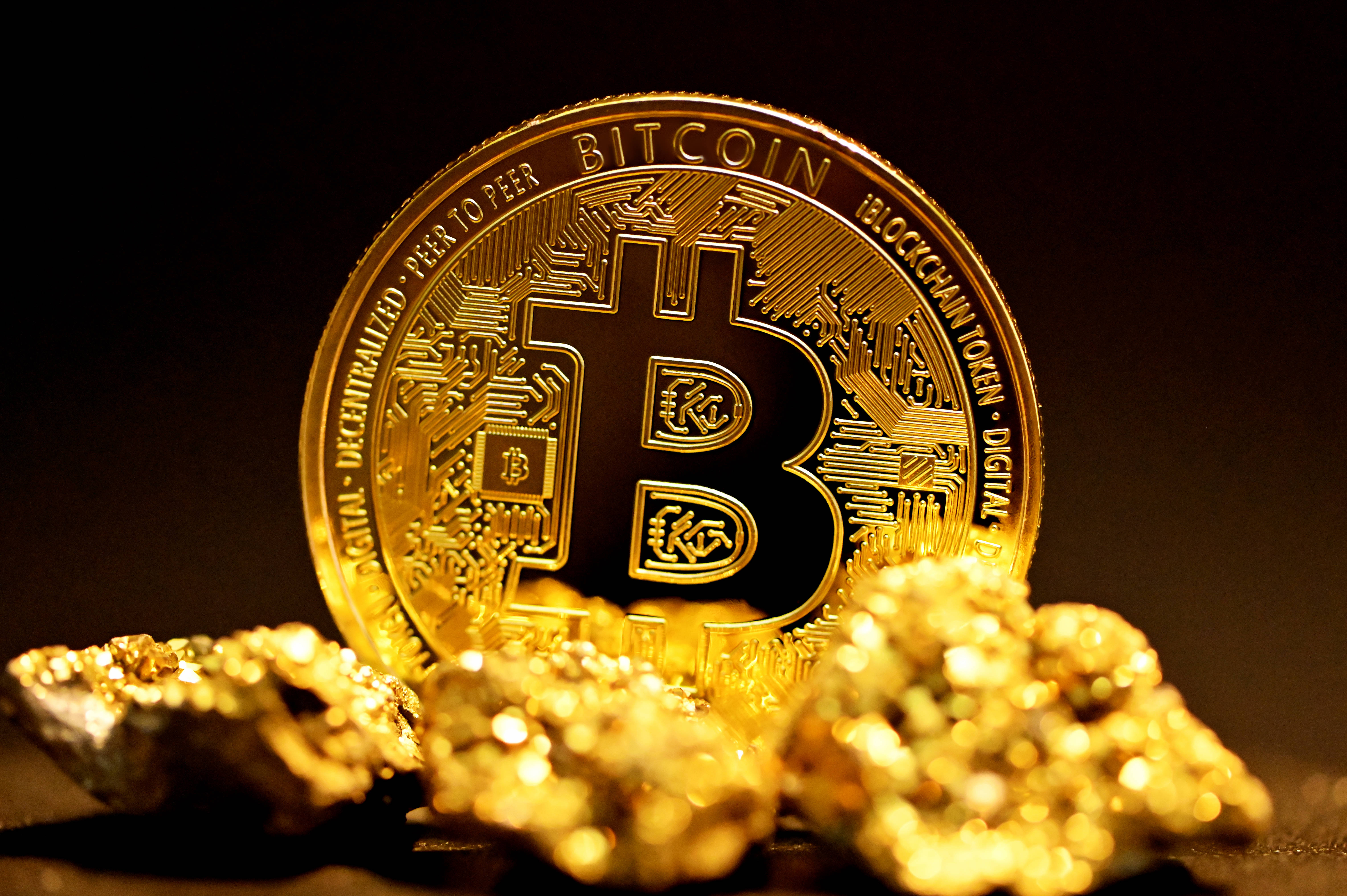比特幣 桌布 壁紙 — 一枚閃閃發光的金色比特幣硬幣放在粗糙的金塊上，在黑暗背景下呈現戲劇性的燈光效果。