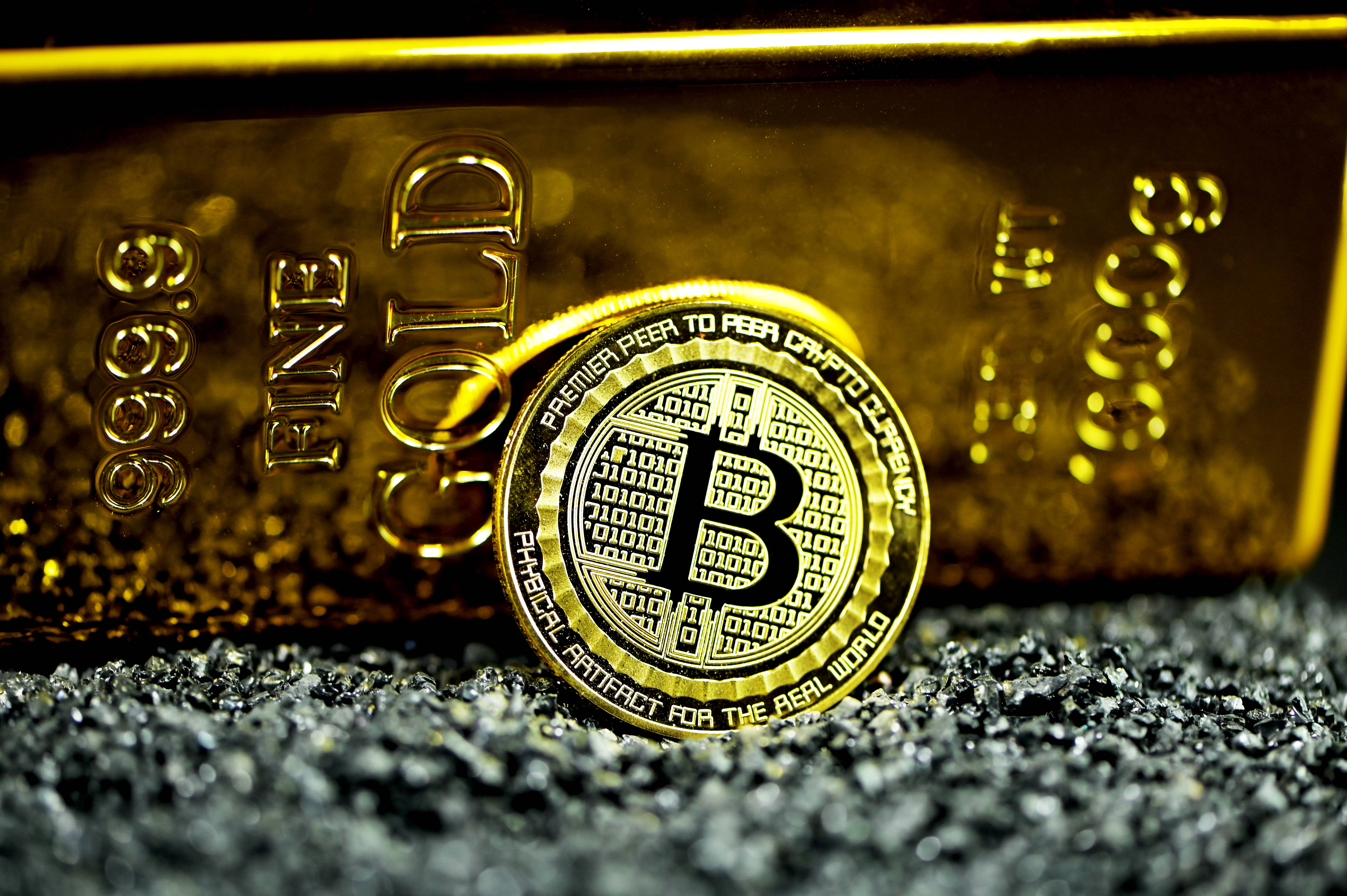 Cryptocurrency 桌布 壁紙 — 一枚閃閃發光的金色比特幣硬幣放在深色礫石上，前面是一塊拋光的金條，上面刻有「FINE GOLD 999.9」。