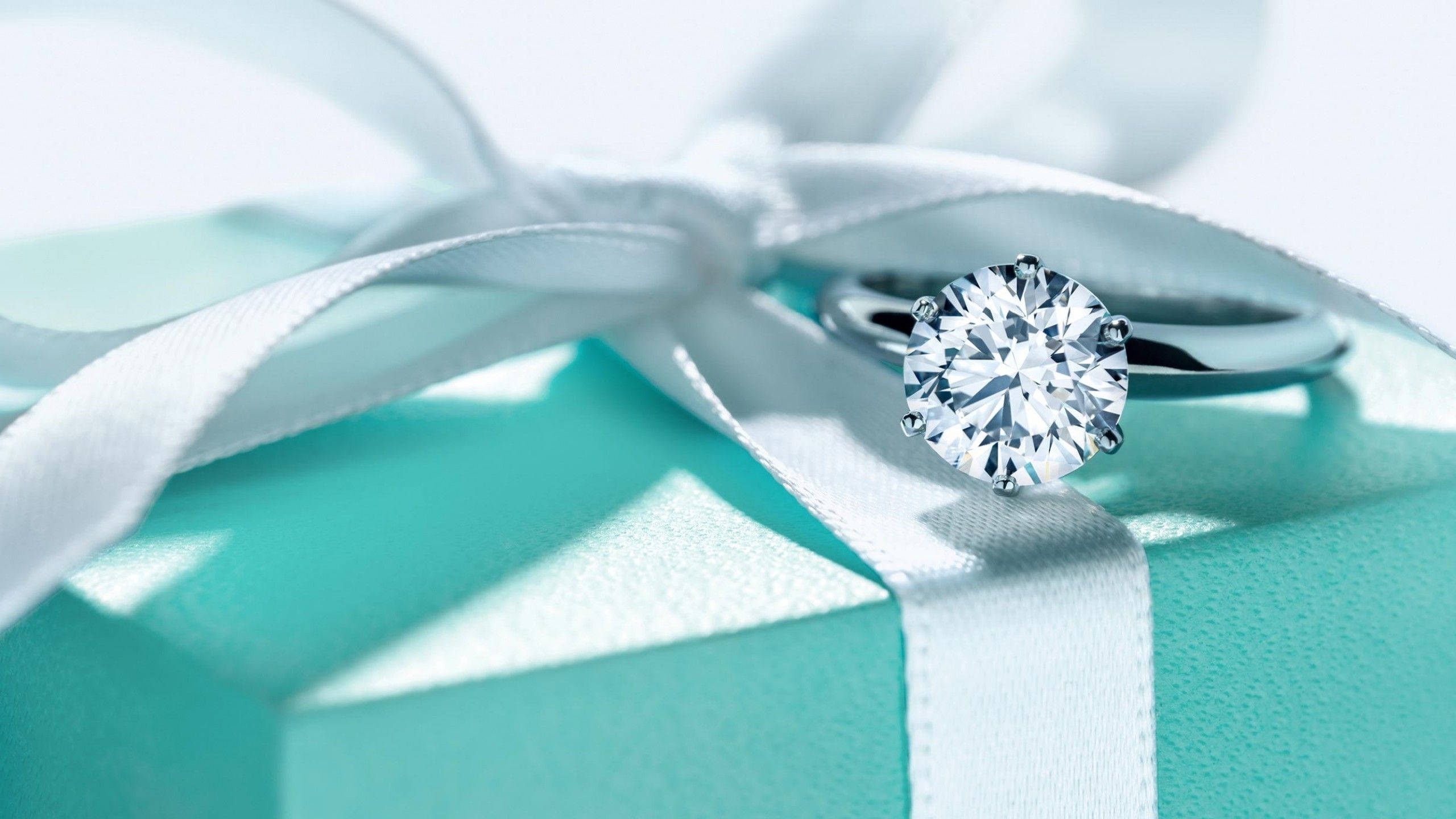 tiffany 桌布 壁紙 — 一枚閃閃發光的鑽石戒指優雅地放在一個標誌性的Tiffany藍色禮物盒上，盒子上繫著一條純白色的絲帶。
