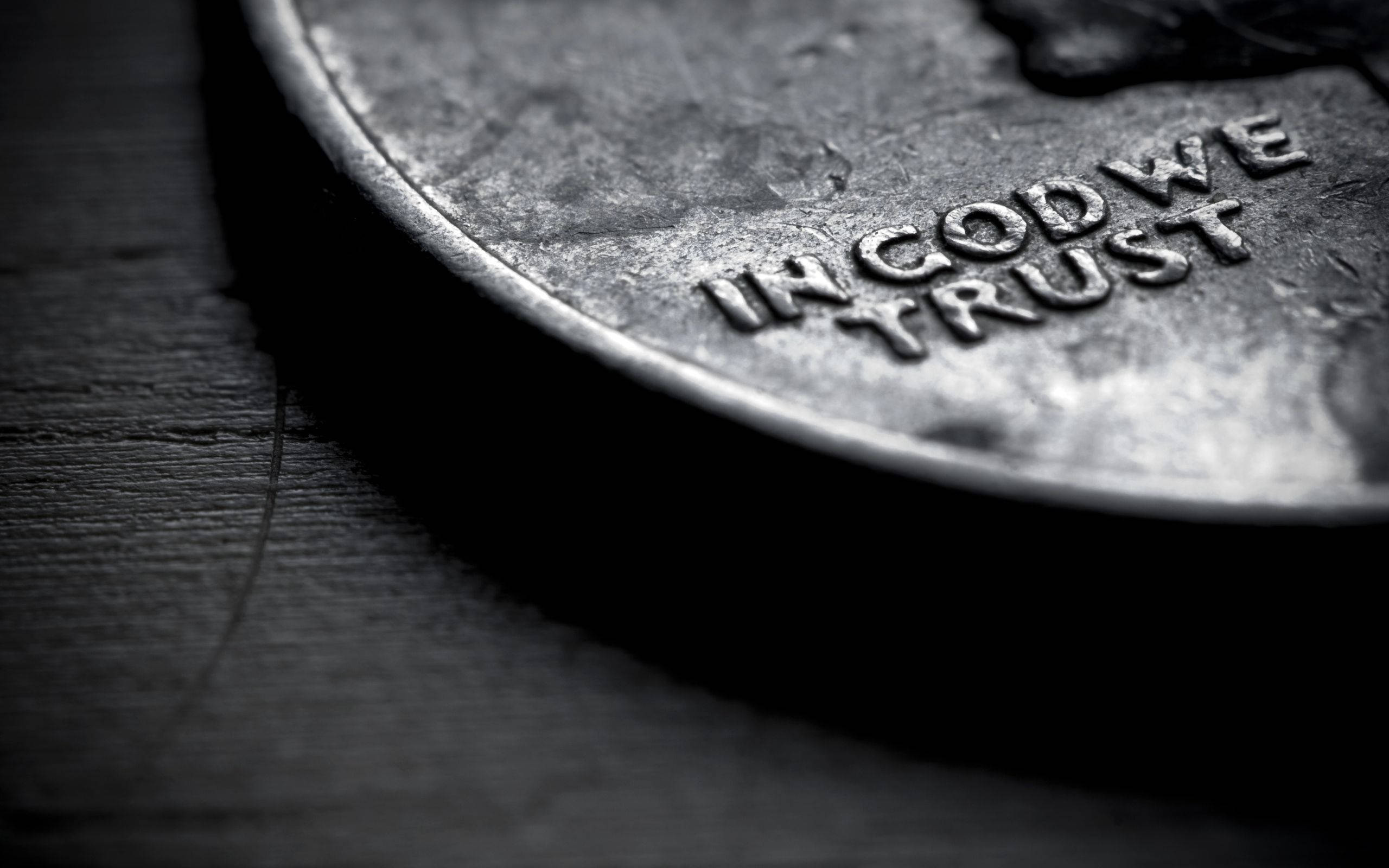 黑白 桌布 壁紙 — 一枚風化的美國一分錢硬幣特寫，上面刻有「IN GOD WE TRUST」，放在深色木頭上，帶有戲劇性的淺景深效果。