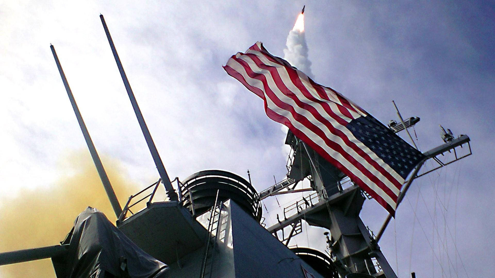 Flag 桌布 壁紙 — 一枚飛彈從海軍軍艦向天空發射，美國國旗在風中飄揚，背景多雲。
