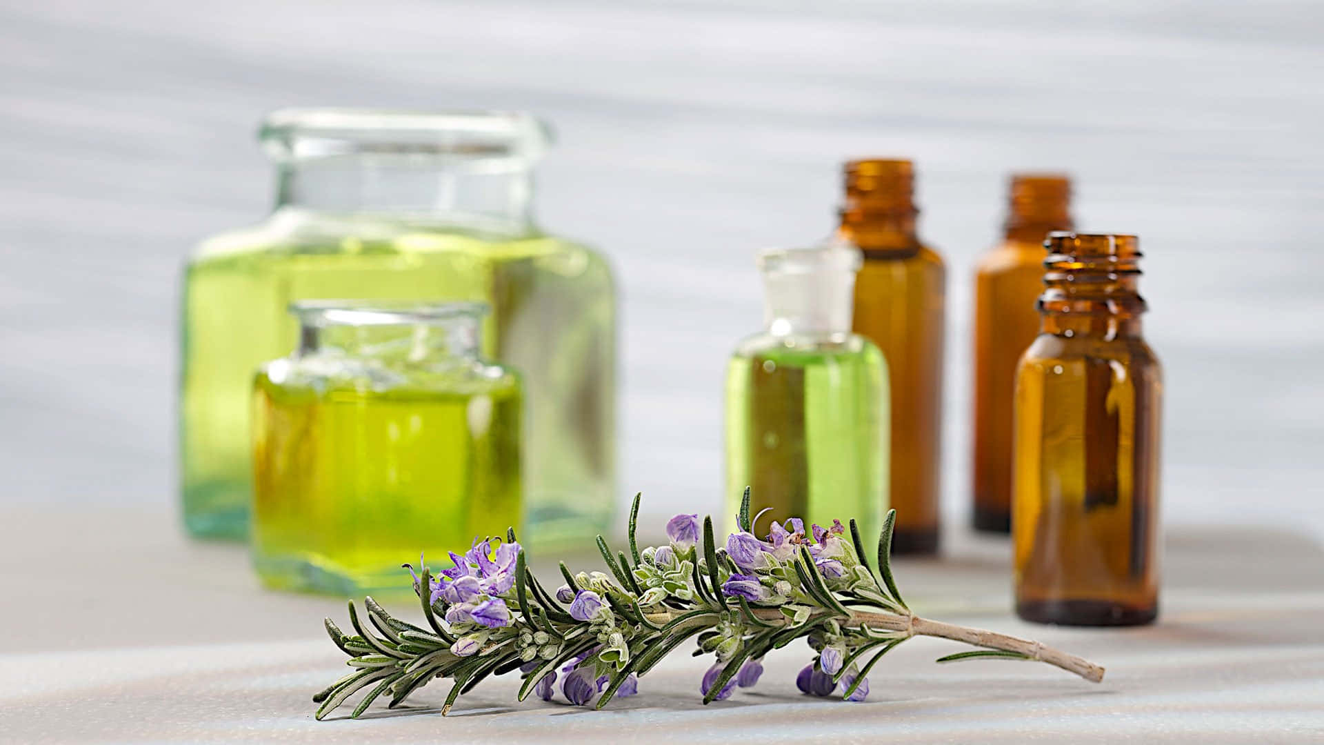 Aromatherapy 桌布 壁紙 — 一枝帶有紫色花朵的薰衣草放在淺色木質表面上，旁邊是裝有綠色液體的琥珀色和玻璃瓶。