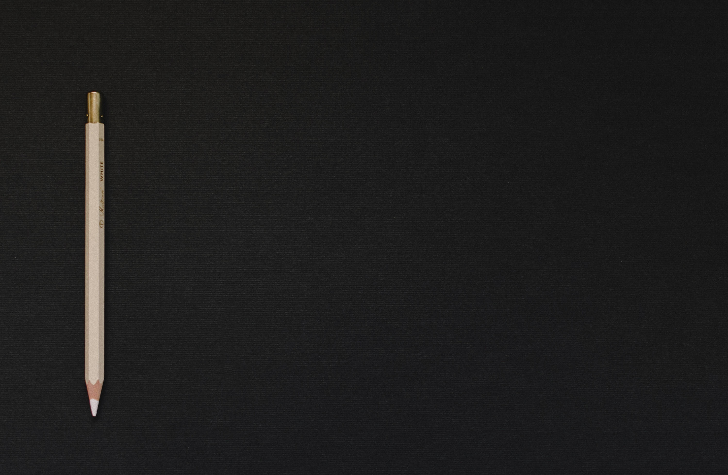 Black Page 桌布 壁紙 — 一枝帶有金色金屬箍的白色鉛筆垂直放置在帶有紋理的黑色布料表面上。
